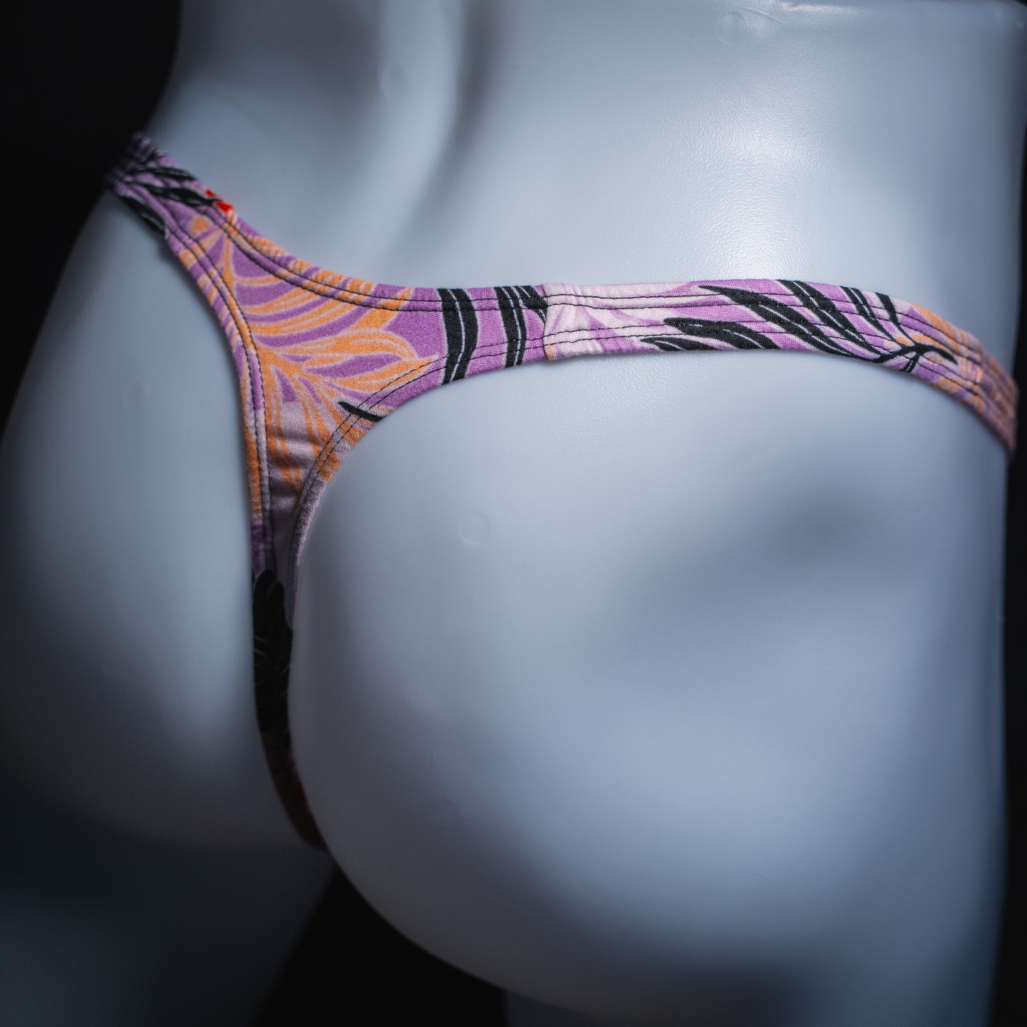 Men's vintage purple Hawaiian floral thong, slim cut, angled rear view.