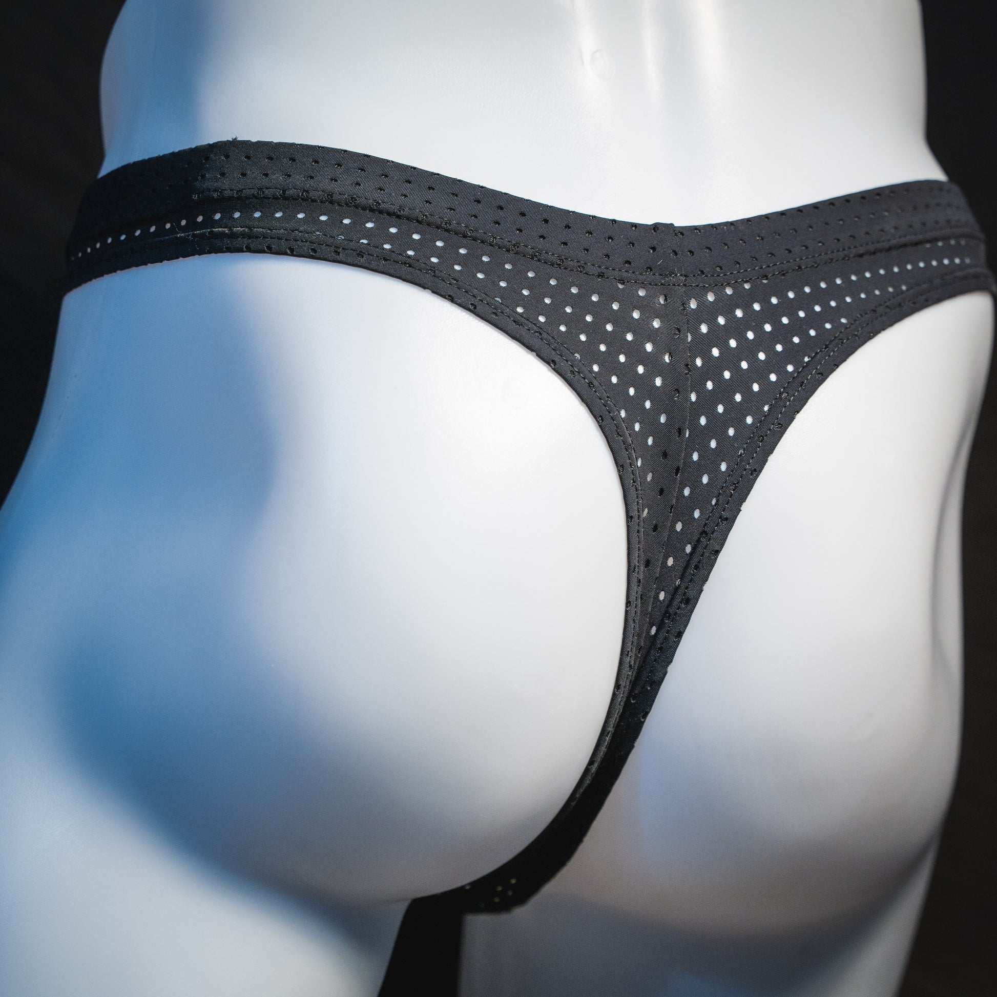 Men's black mesh pre-release thong underwear, angled rear view.