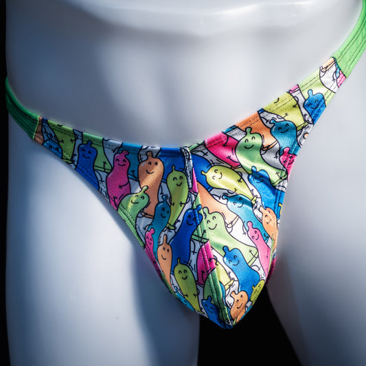 A close-up of a colorful thong-style bikini bottom displayed on a white mannequin torso. The fabric has an allover cartoon ghost print in bright blue, green, pink, yellow, and orange on a white base, with a solid neon green waistband.