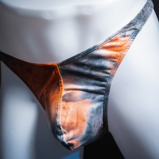 Men's black and red tie dye thong, classic cut, angled front view.