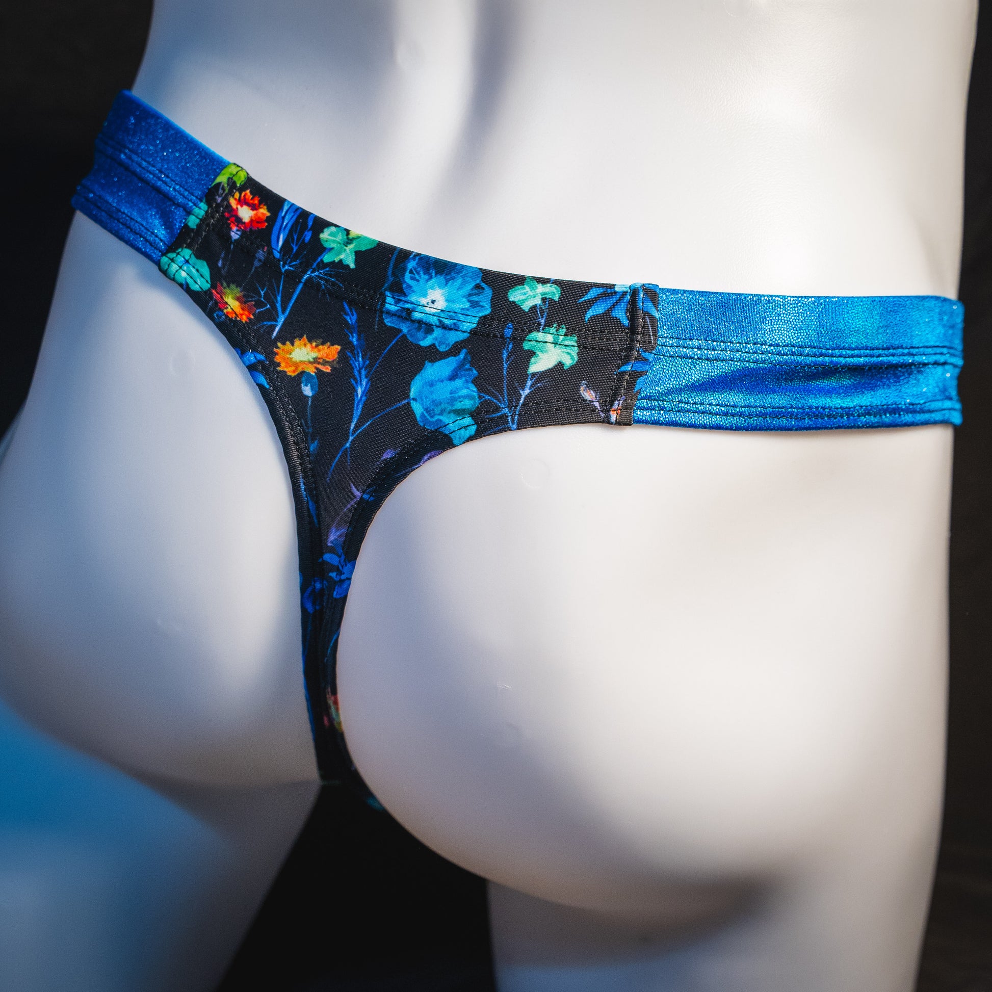 Men's floral thong underwear with metallic blue straps, robust cut, angled rear view.