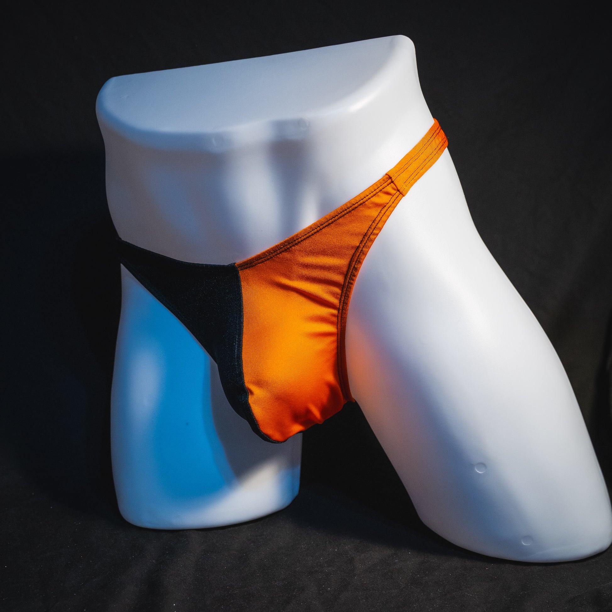 Men's orange and black asymmetrical Halloween thong, classic cut, angled full front view.