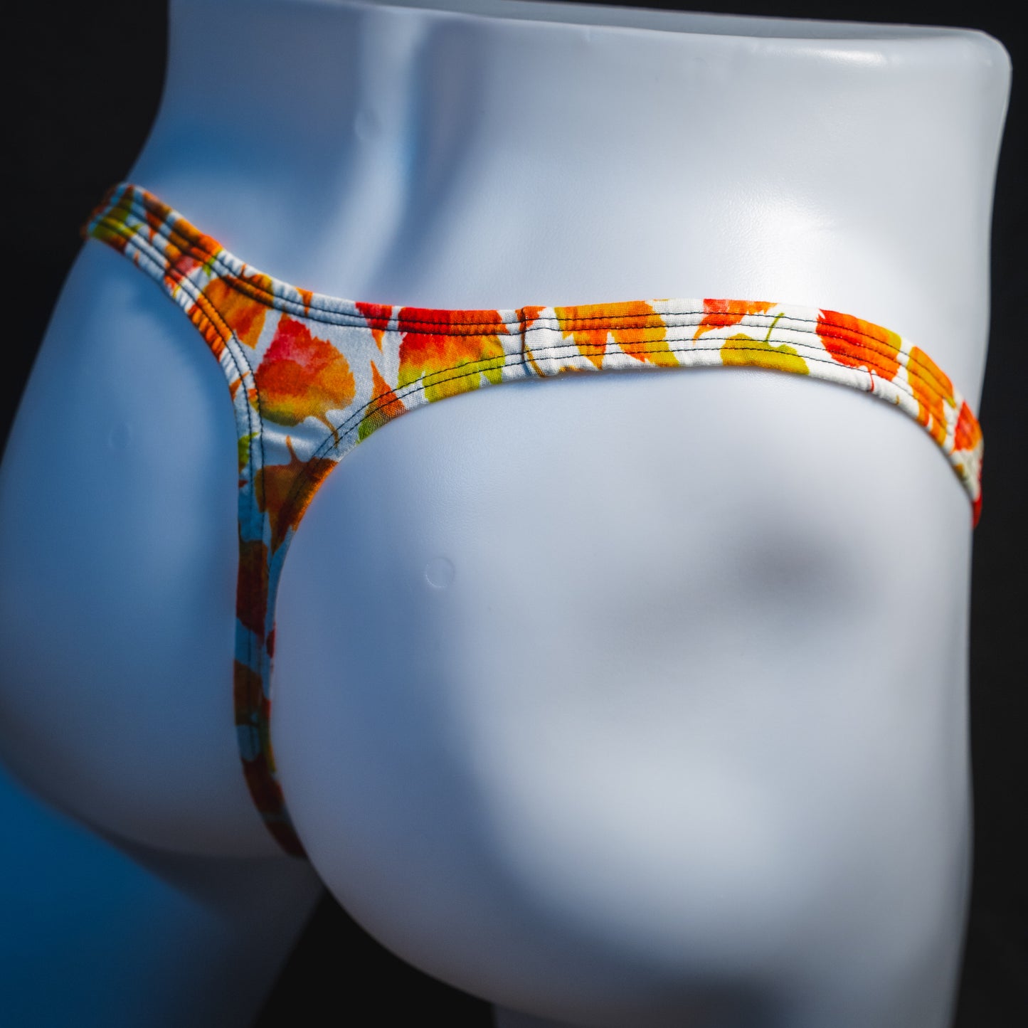 Men's orange autumn leaves thong underwear, classic cut, angled rear view.