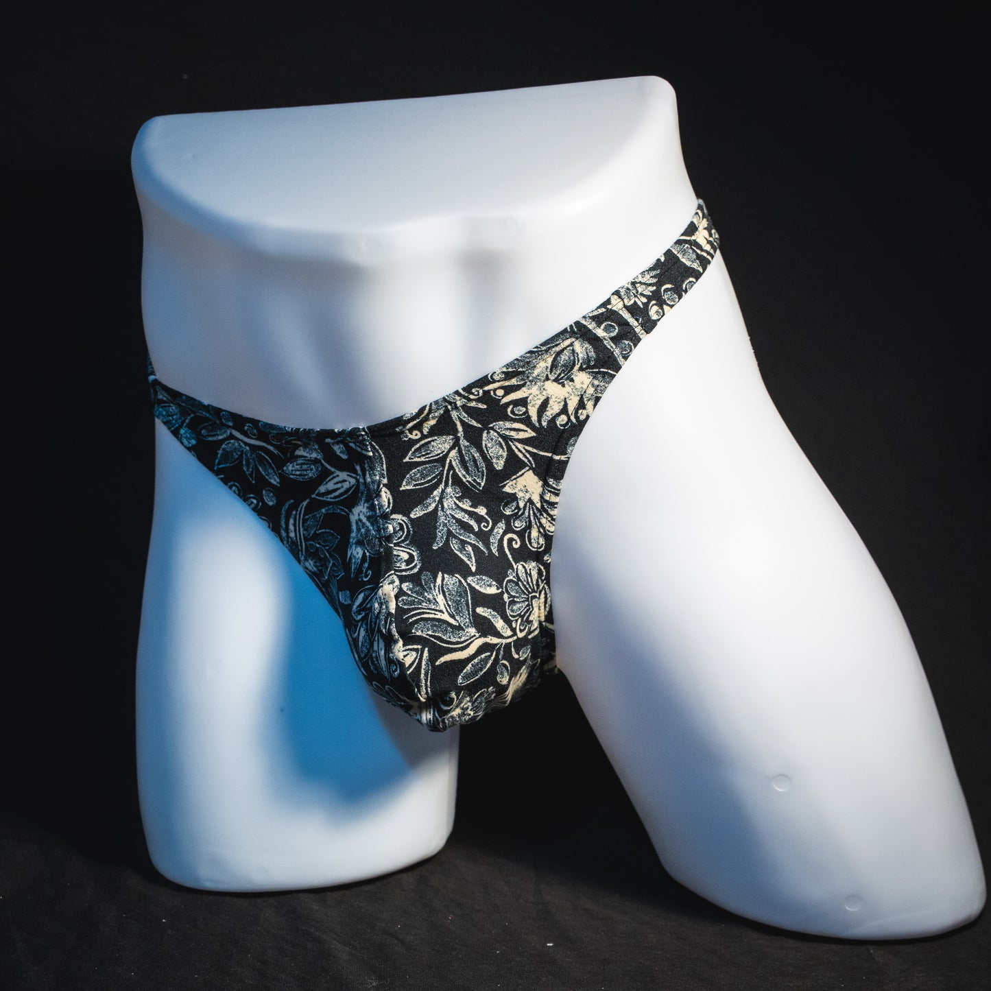 Men's black and white paisley thong underwear, classic cut, angled full front view.