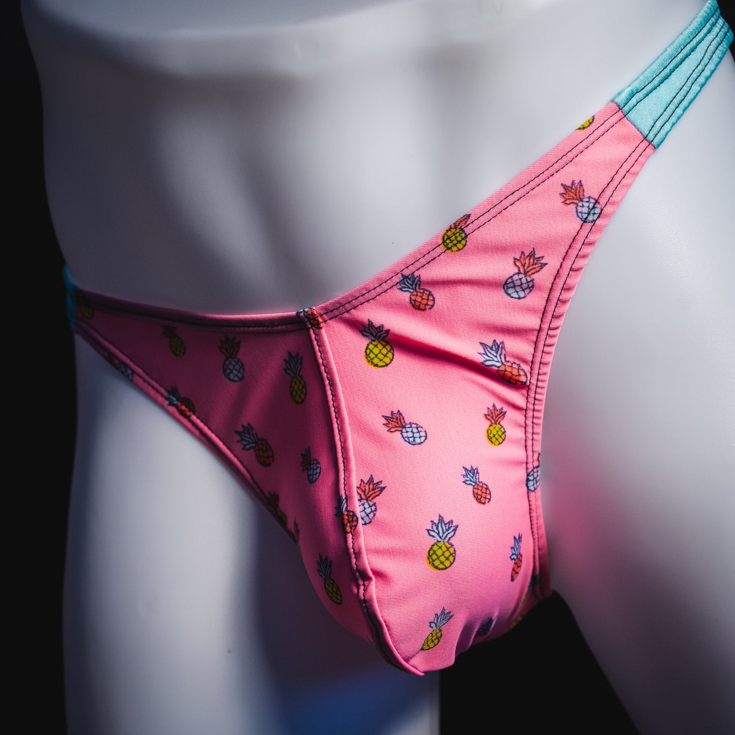 Men's bright pink and blue tropical thong underwear with pineapples, classic cut, angled front view.