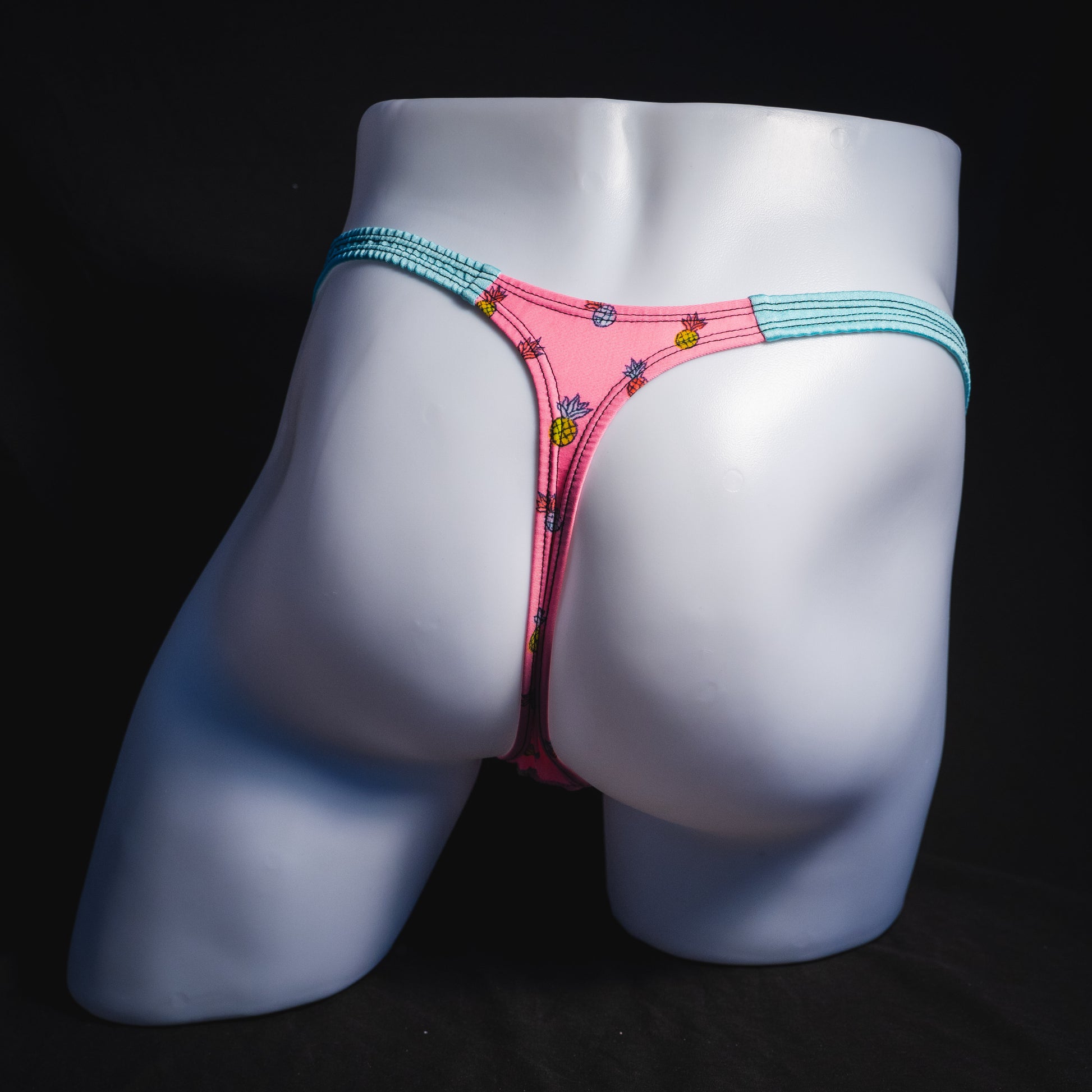 Men's bright pink and blue tropical thong underwear with pineapples, classic cut, full rear view.