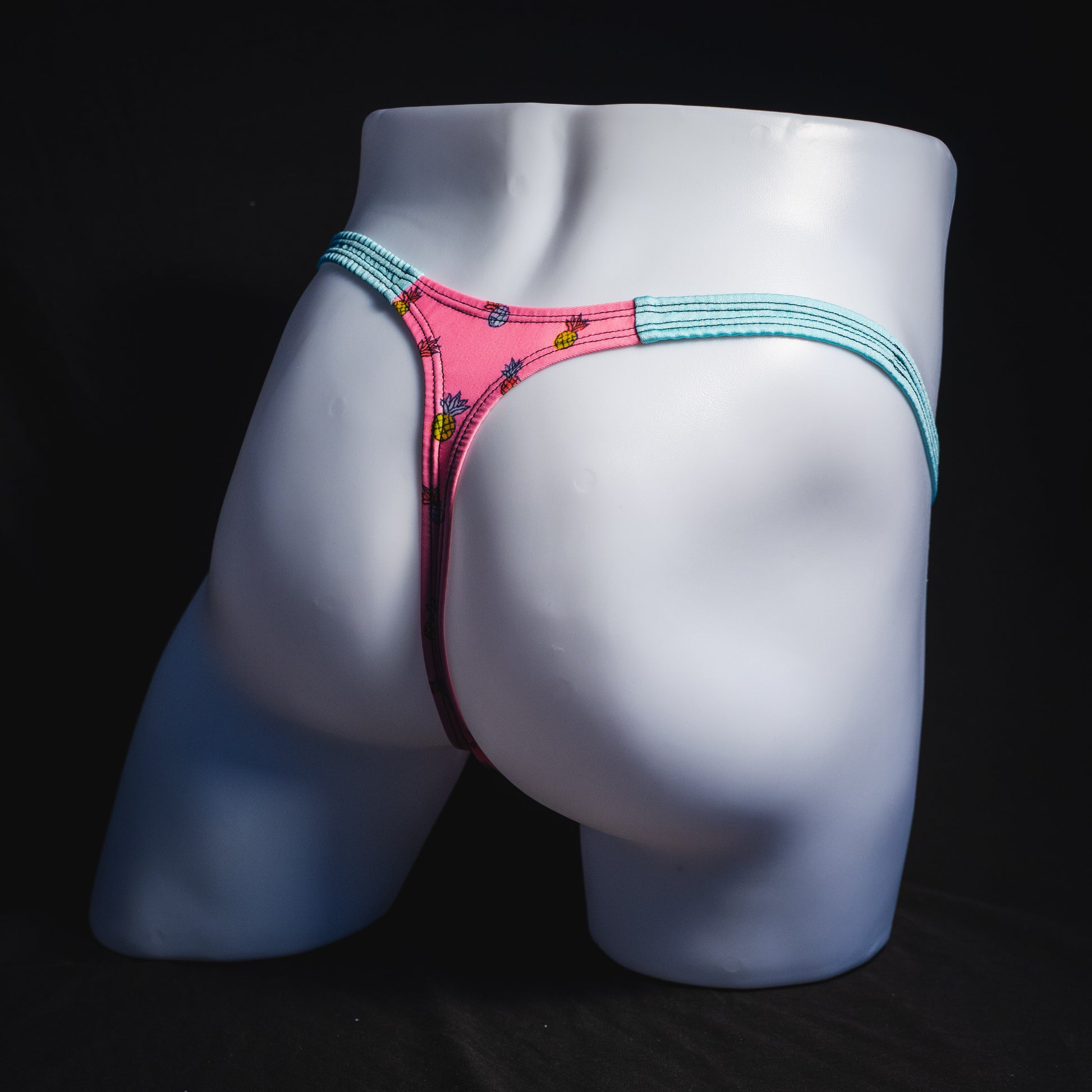 Men's bright pink and blue tropical thong underwear with pineapples, classic cut, full angled rear view.