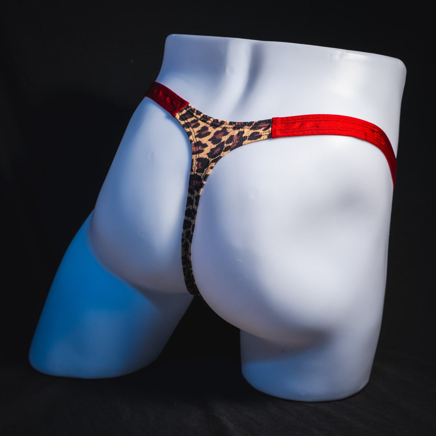 Men's cheetah print thong with red waistband, classic cut, full angled rear view.