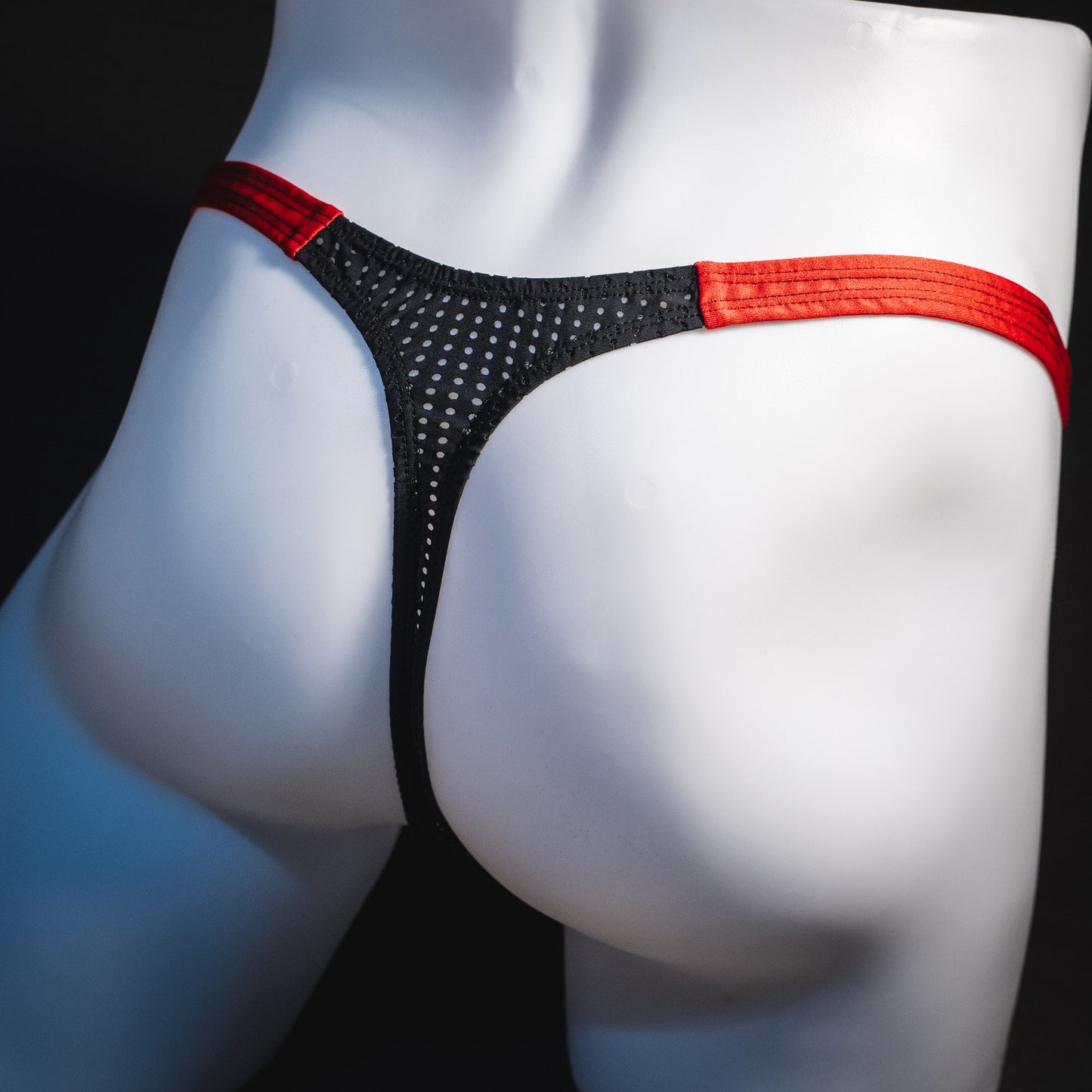Men's black and red mesh thong underwear, classic cut, angled rear view.