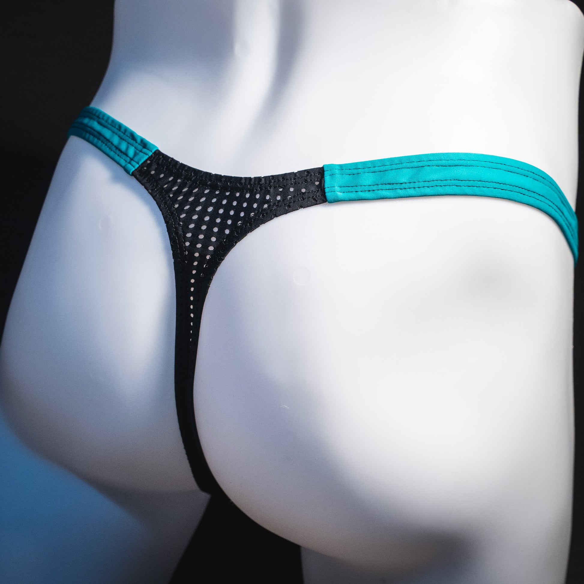 Black mesh with teal waistband, men's thong underwear, tower cut, angled rear view.