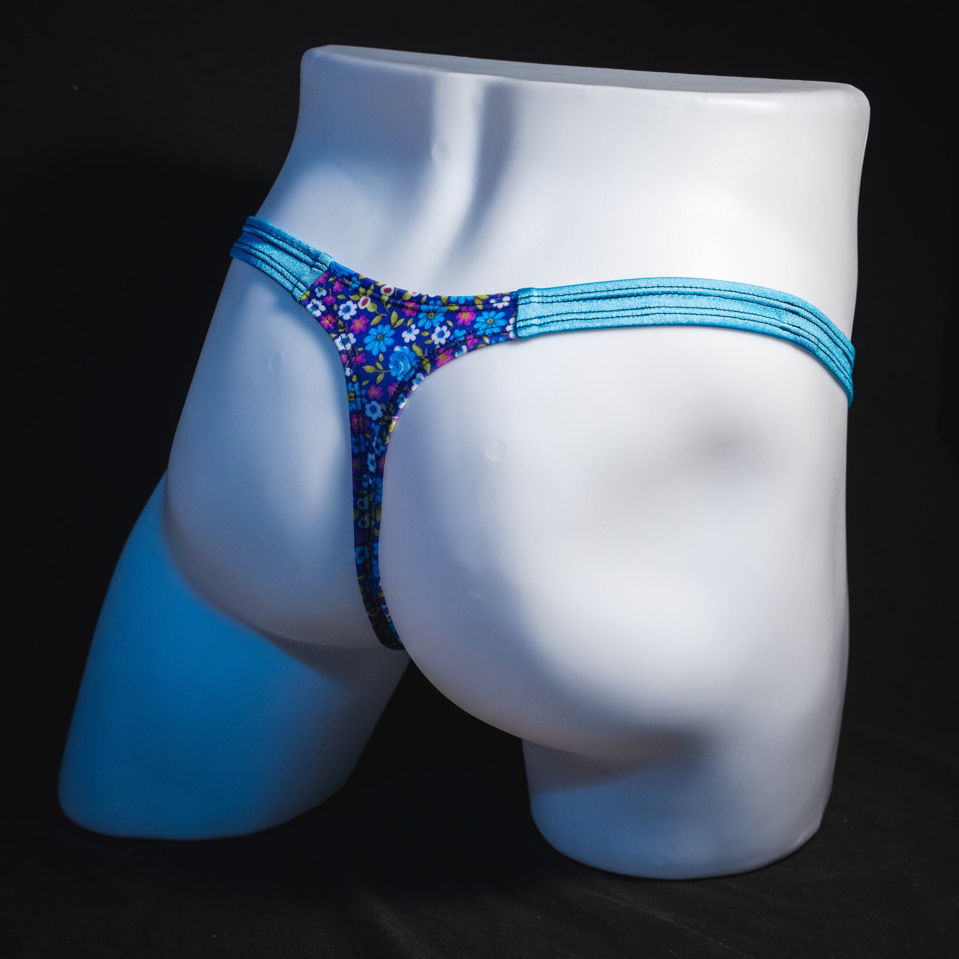 Men's blue and purple flower patch thong underwear, classic cut, angled full rear view.