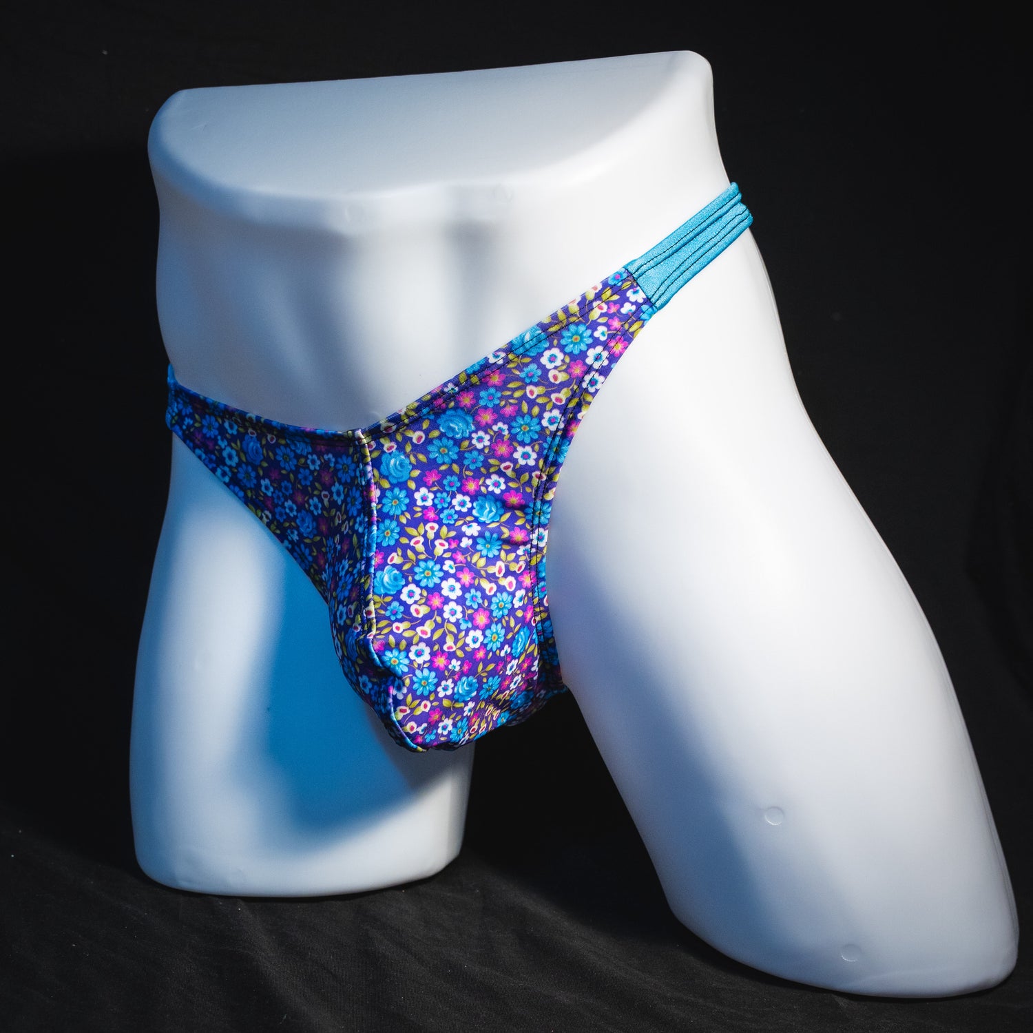 Men's blue and purple flower patch thong underwear, classic cut, angled full front view.
