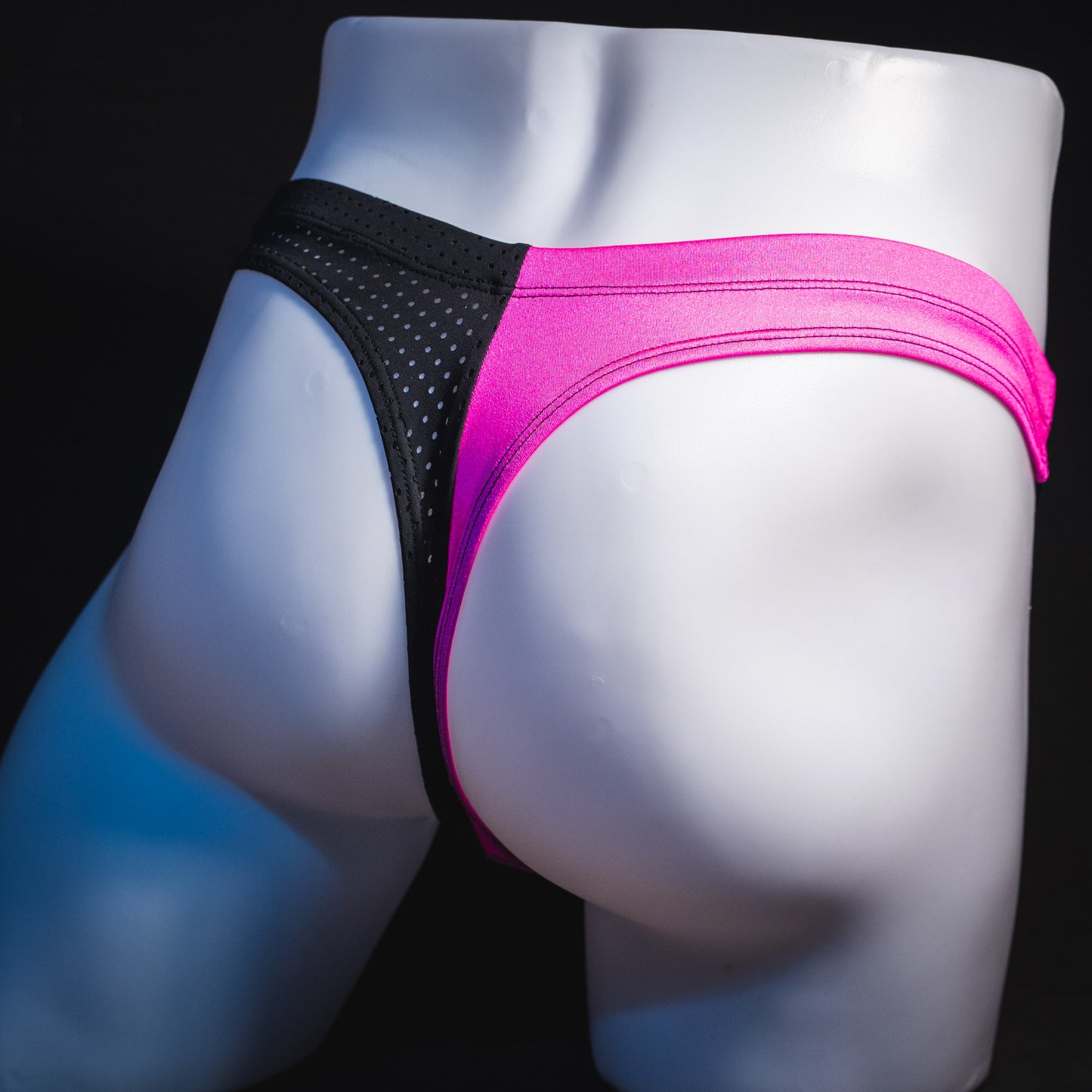Men's bright pink and black mesh thong underwear, angled rear view.