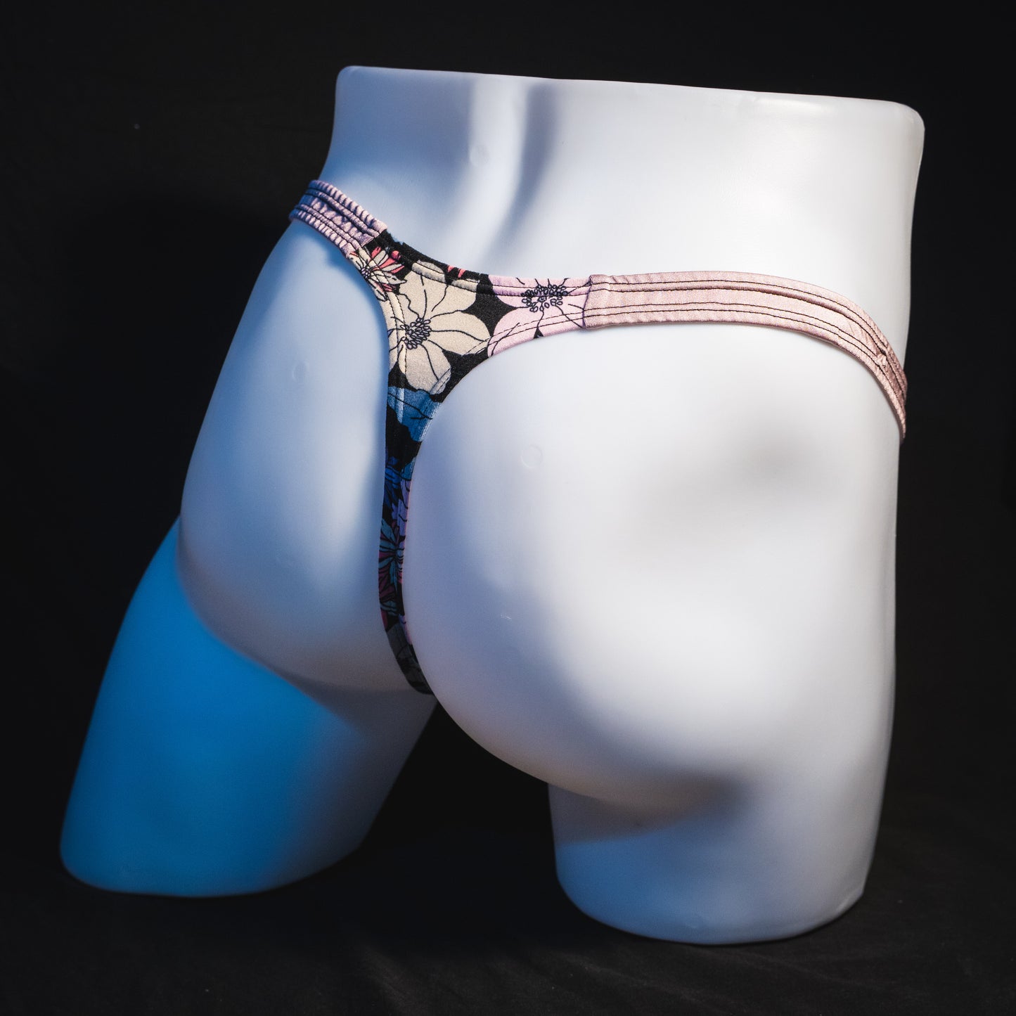 Men's purple floral with lilac straps thong underwear, classic cut, full angled rear view.