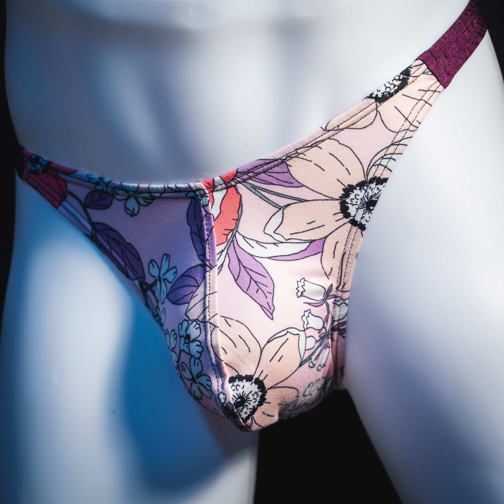 Men's purple floral thong underwear, classic cut, angled front view.