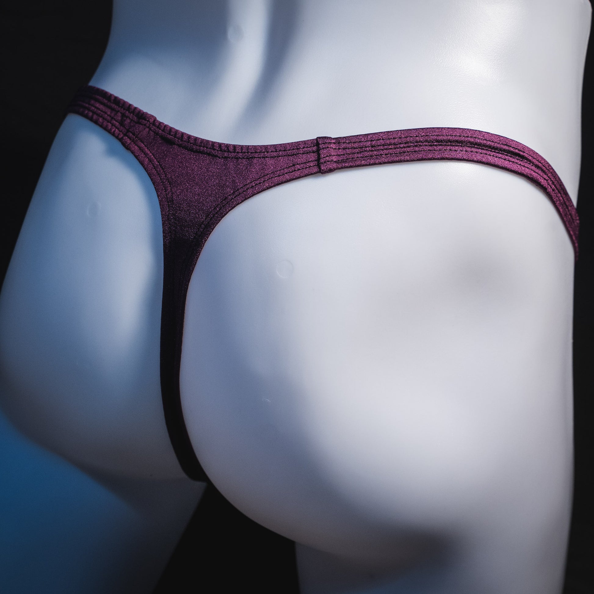 Men's solid purple thong underwear, classic cut, angled rear view.