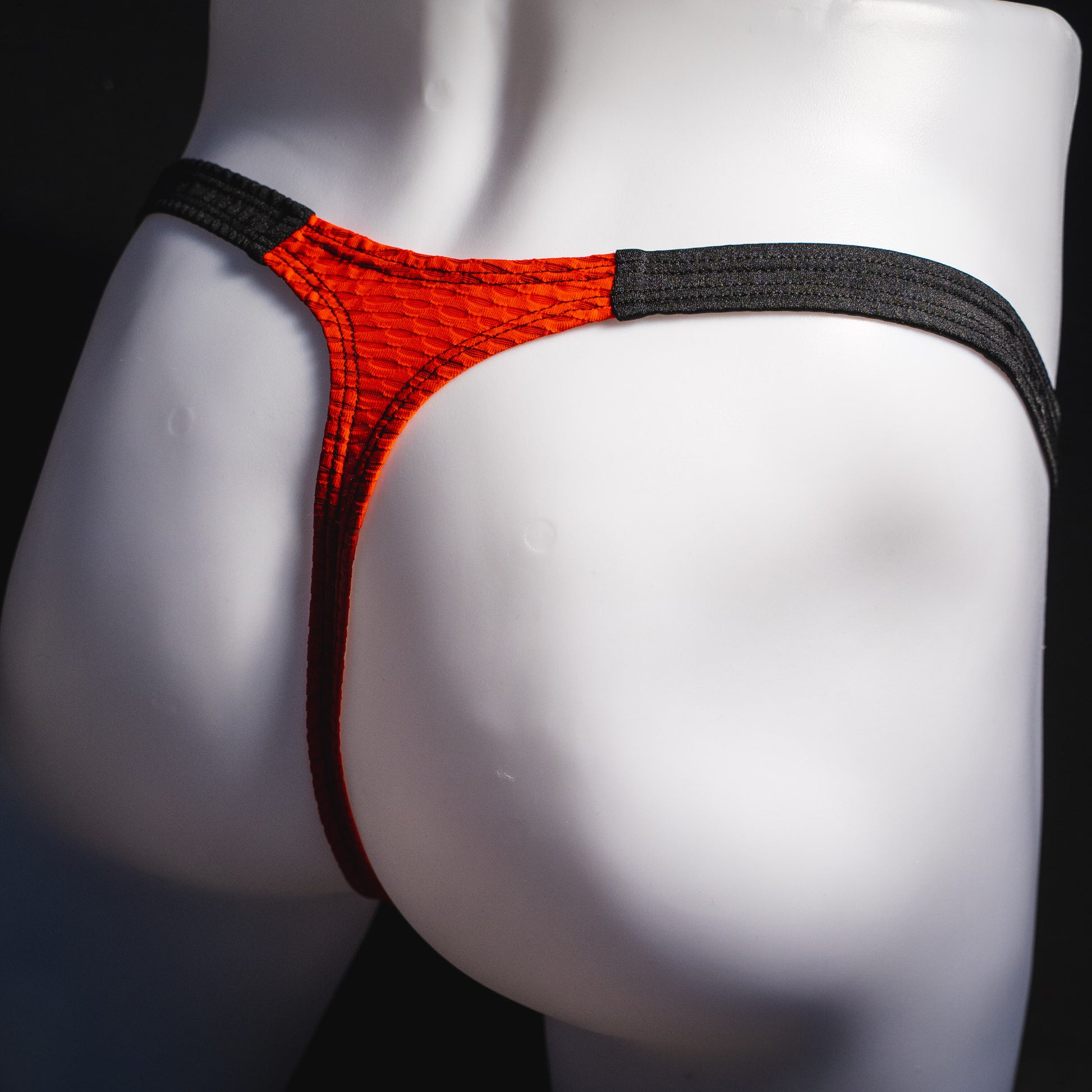 Men's red and black athletic mesh thong underwear, classic cut, angled rear view.