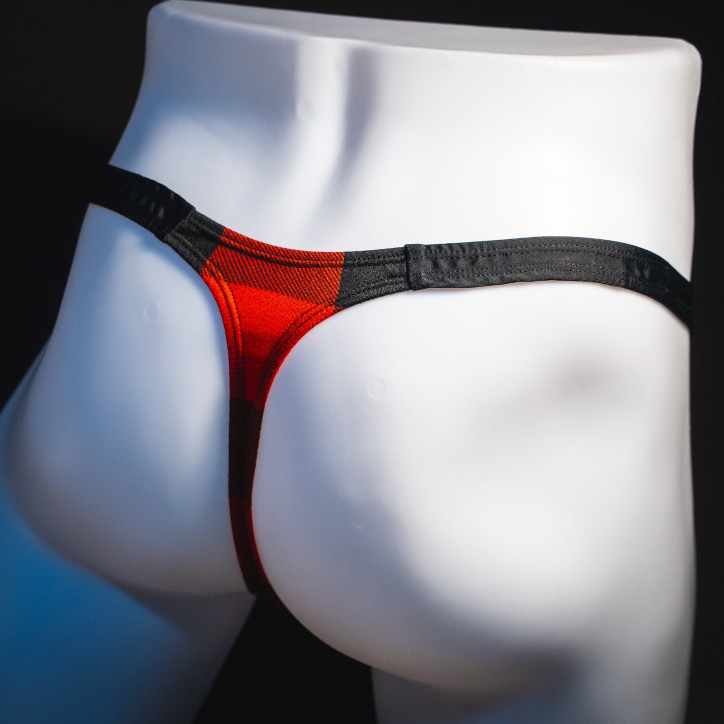 Men's red plaid with black straps thong underwear, classic cut, angled rear view.