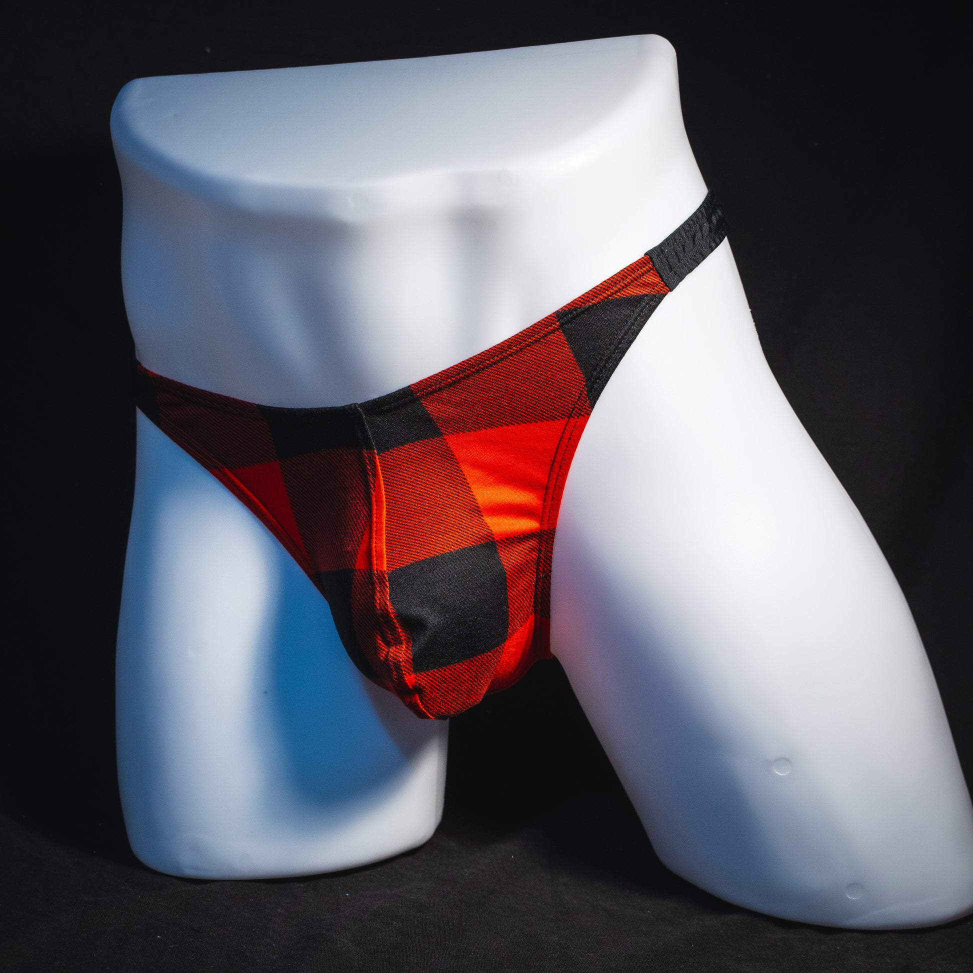 Men's red plaid with black straps thong underwear, classic cut, angled full front view.