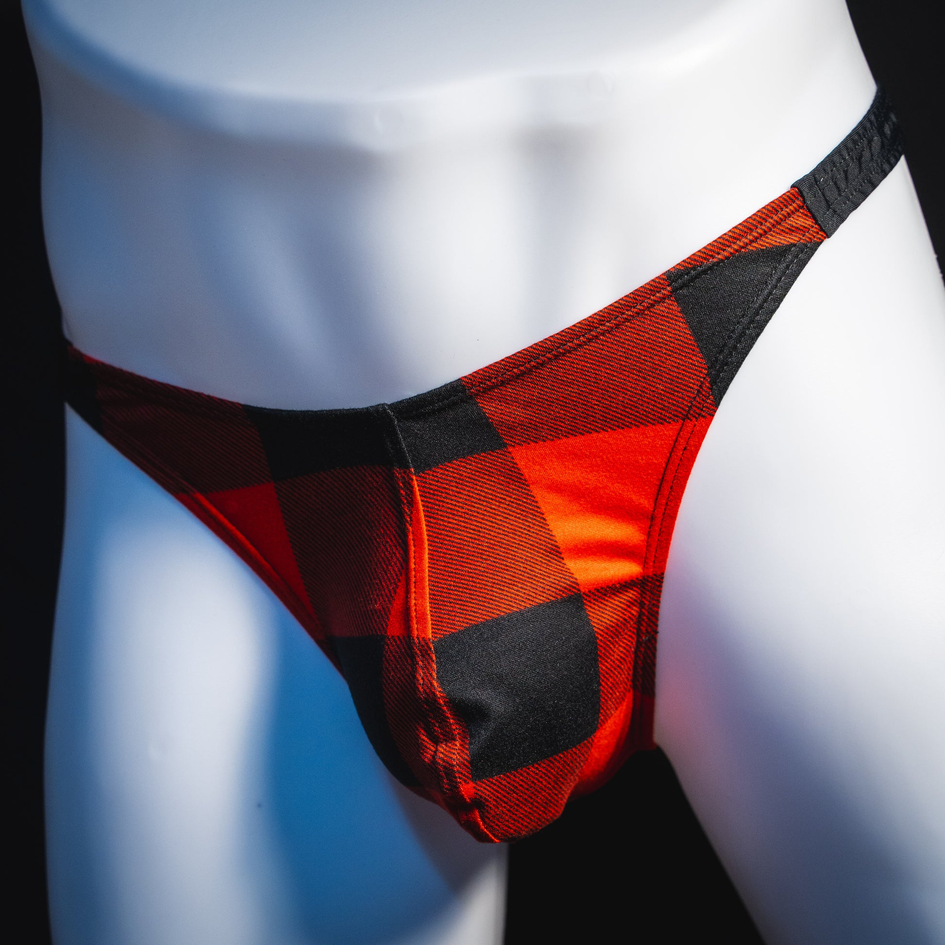 Men's red plaid with black straps thong underwear, classic cut, angled front view.