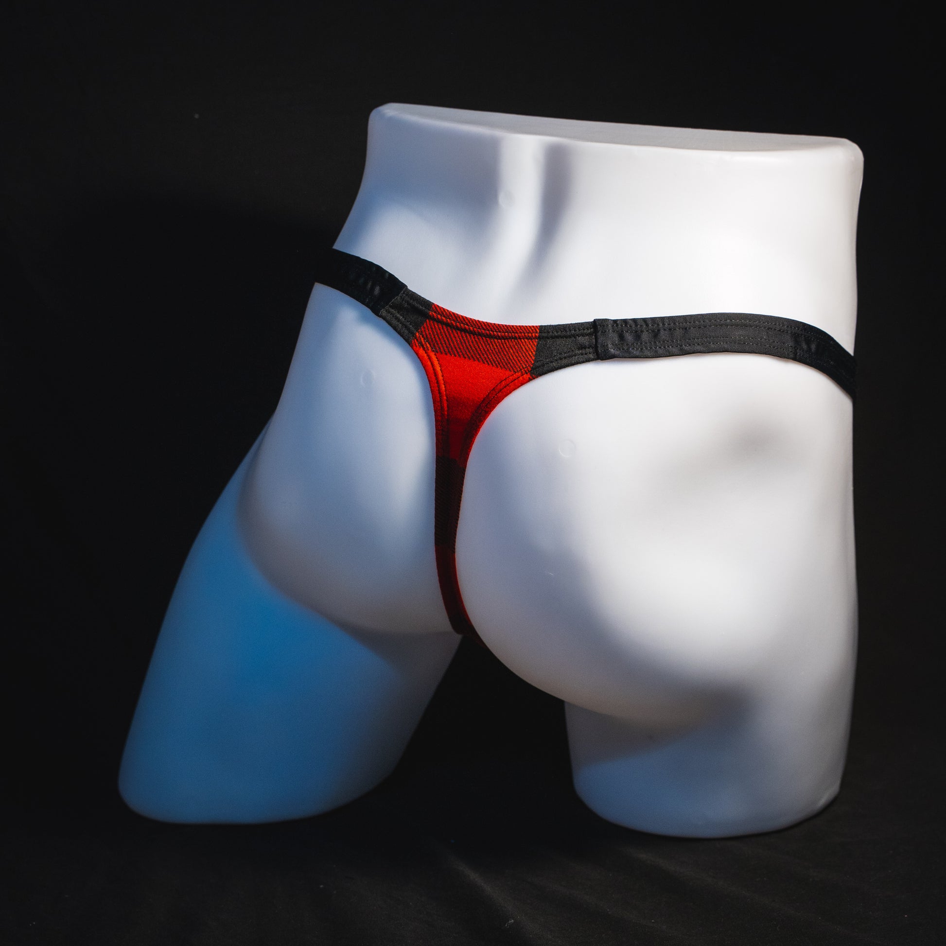 Men's red plaid with black straps thong underwear, classic cut, angled full rear view.
