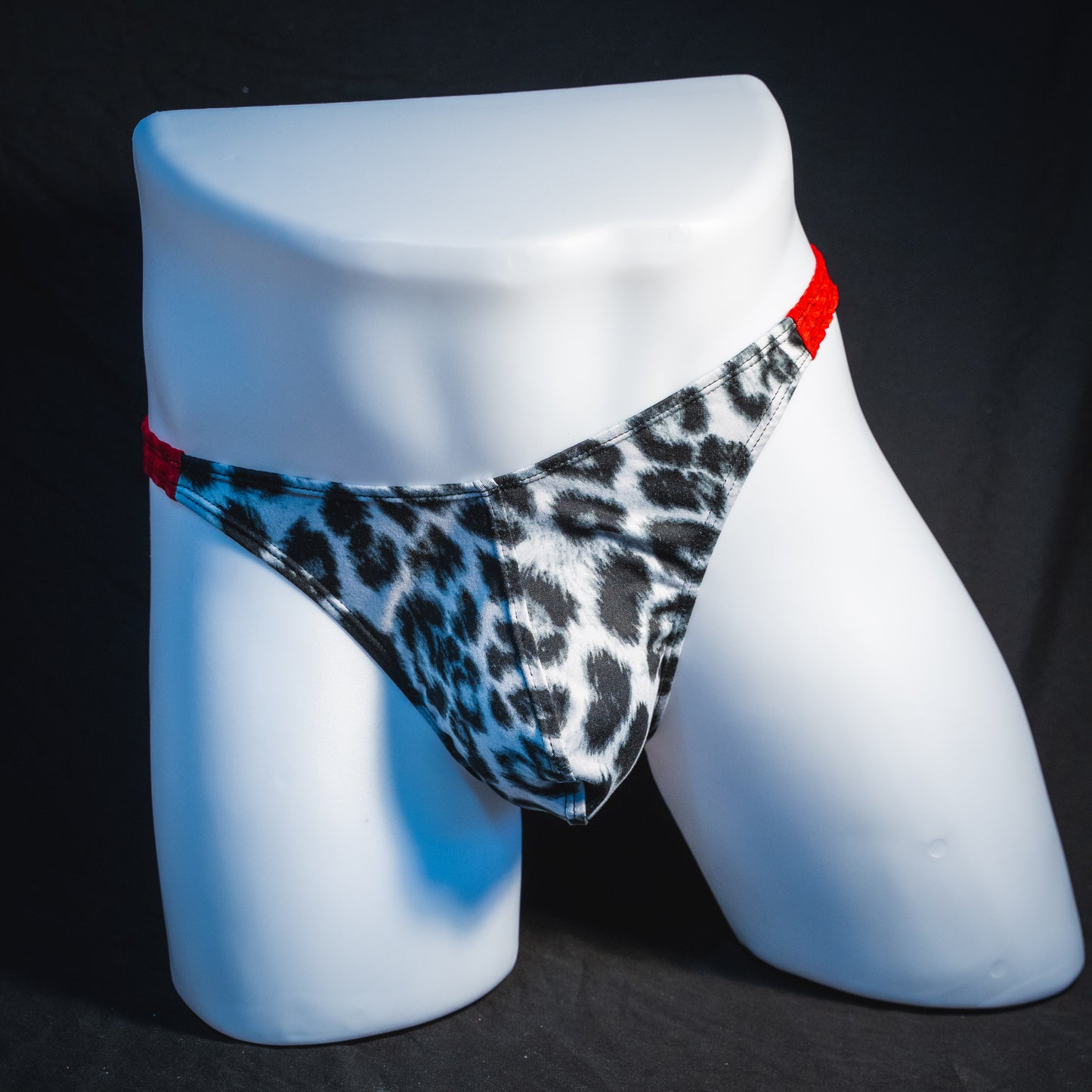 Men's black and white leopard thong underwear with textured red straps, classic cut, full front view.