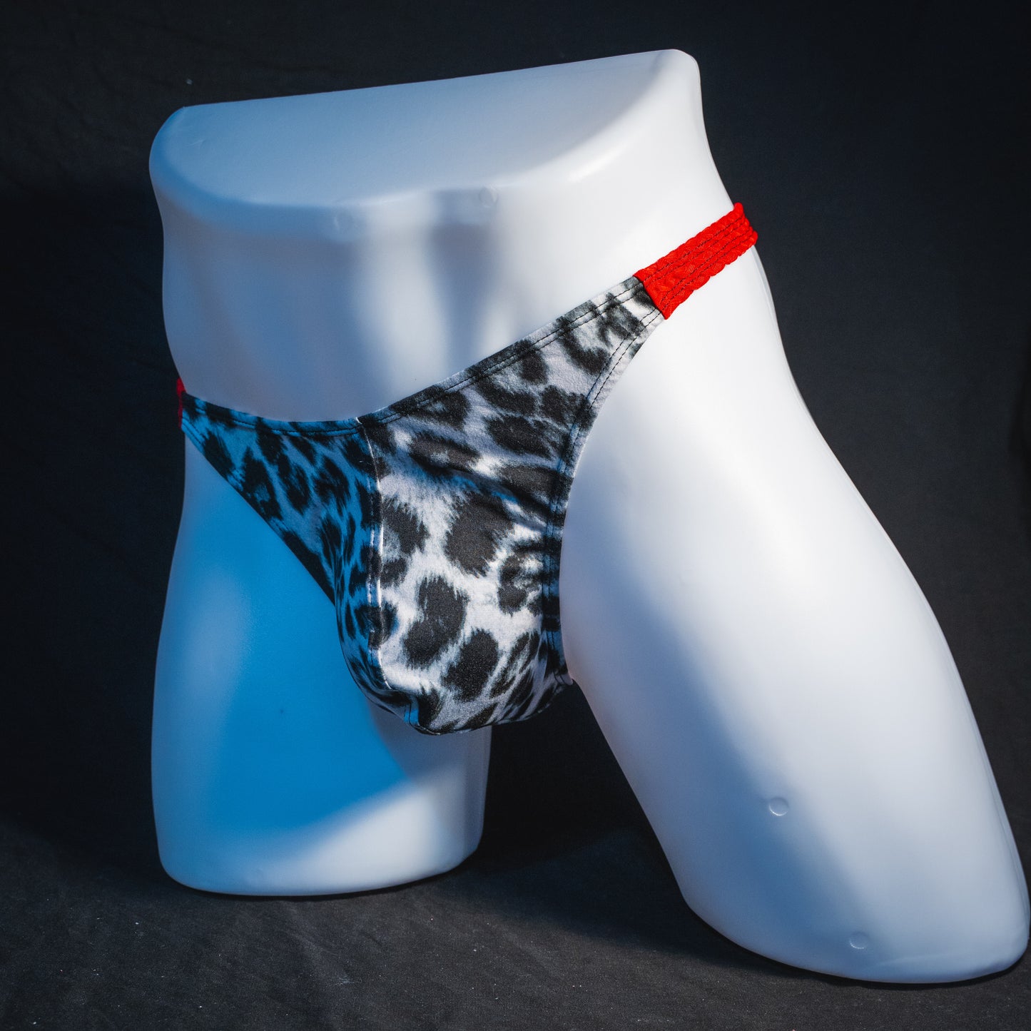 Men's black and white leopard thong underwear with textured red straps, classic cut, angled full front view.