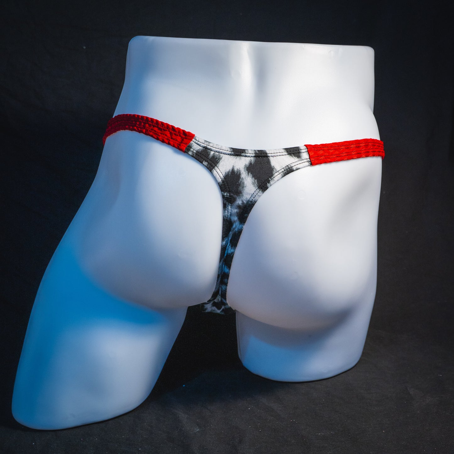 Men's black and white leopard thong underwear with textured red straps, classic cut, full rear view.