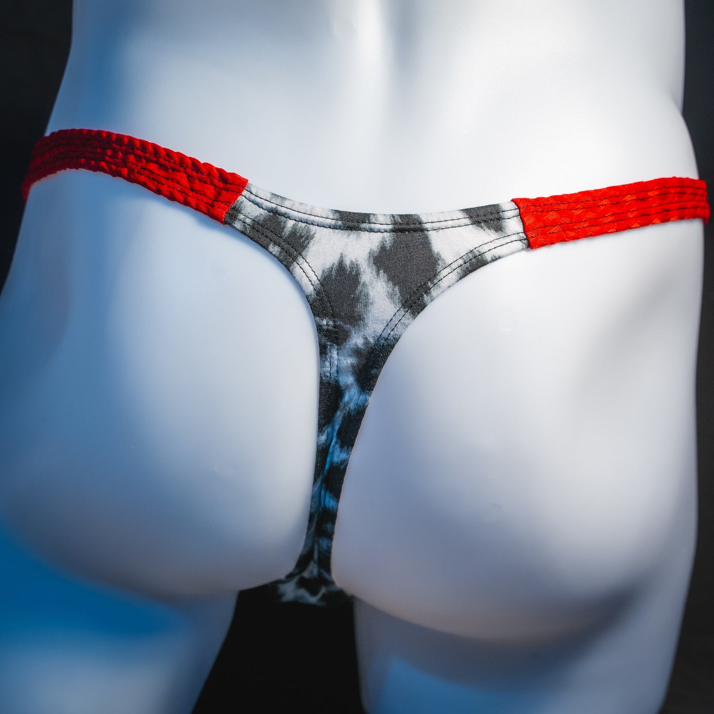 Men's black and white leopard thong underwear with textured red straps, classic cut, rear view.