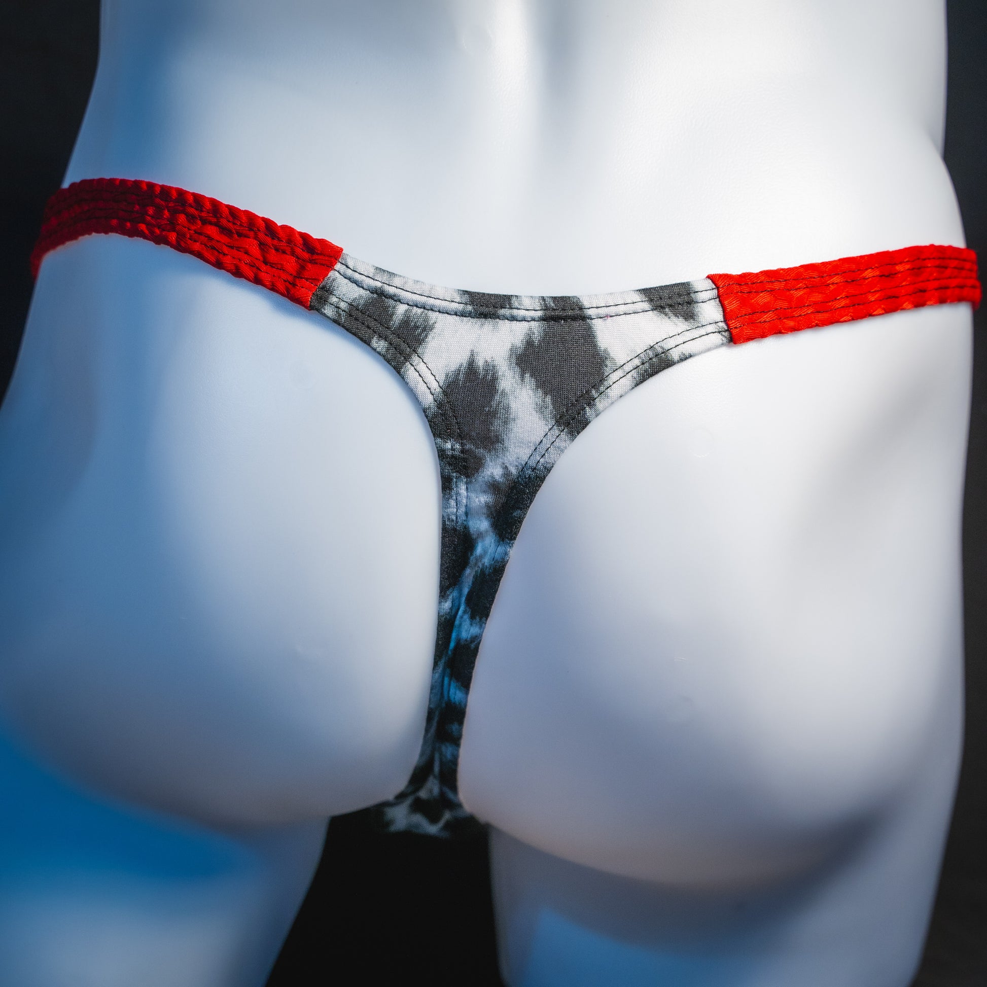 Men's black and white leopard thong underwear with textured red straps, classic cut, rear view.
