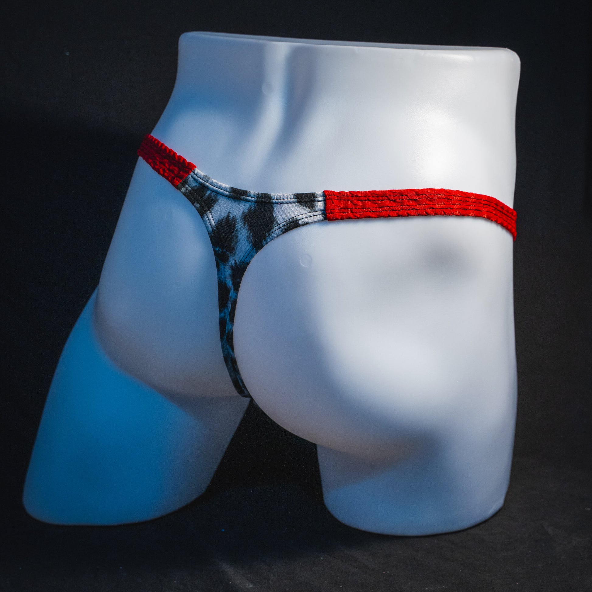 Men's black and white leopard thong underwear with textured red straps, classic cut, full angled rear view.