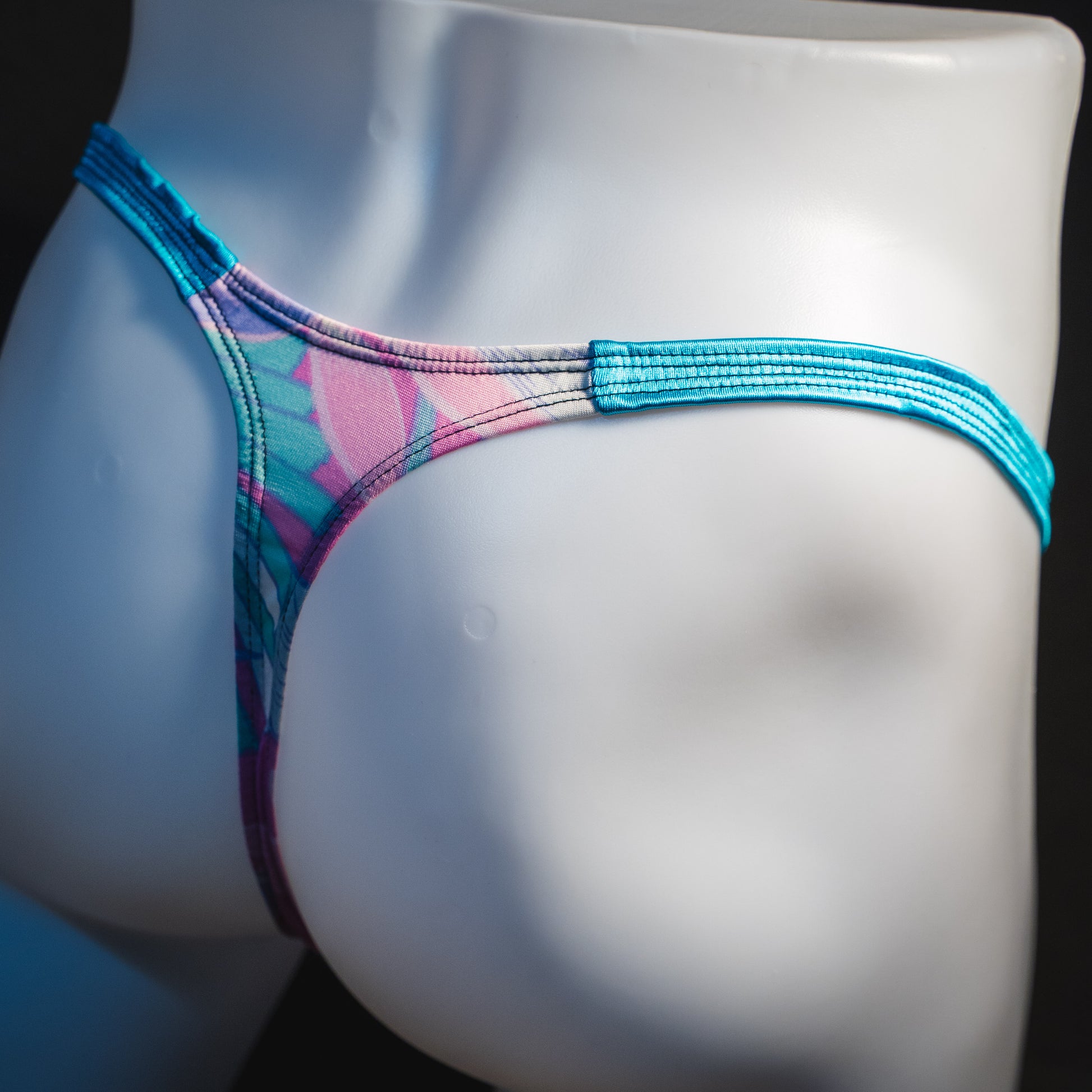Men's pink and blue feathers thong underwear, classic cut, angled rear view.