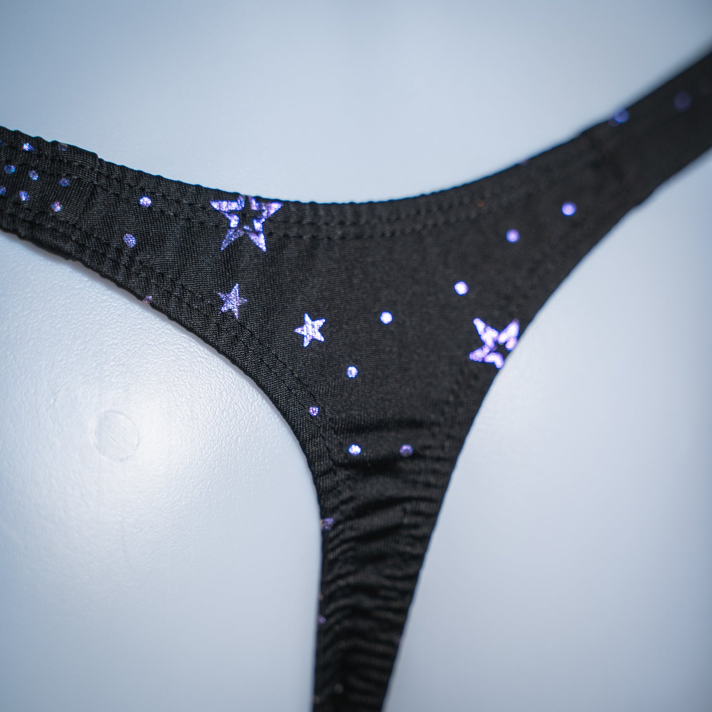 Men's black with purple foil moons and stars thong, classic cut, rear closeup view.