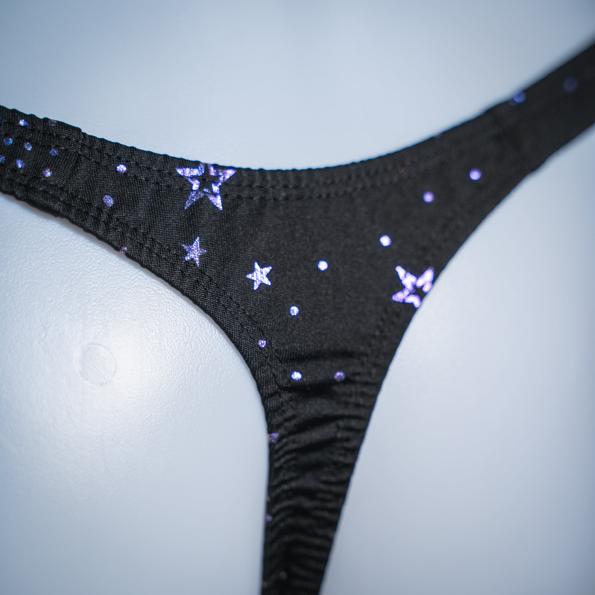 Men's black with purple foil moons and stars thong, classic cut, rear closeup view.