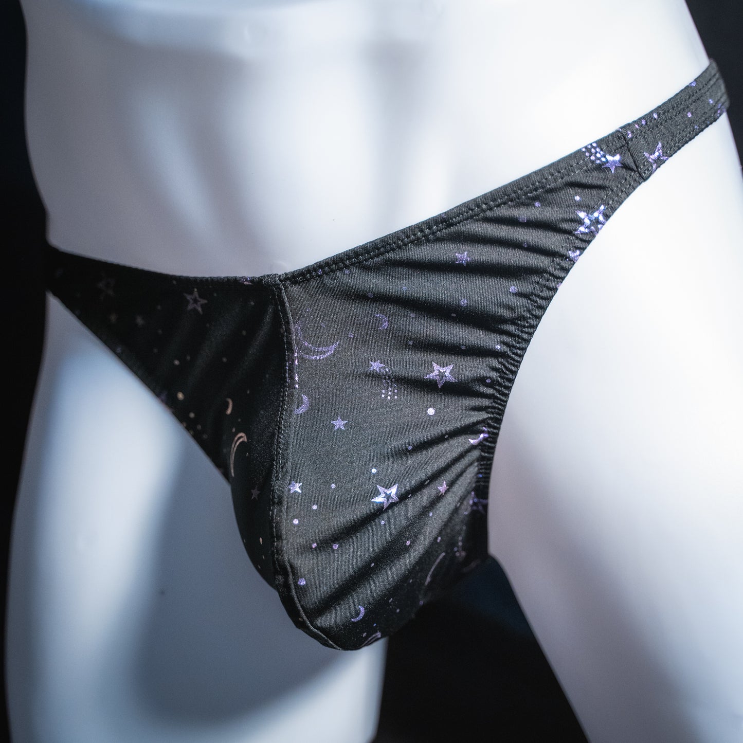 Men's black with purple foil moons and stars thong, classic cut, angled front view.