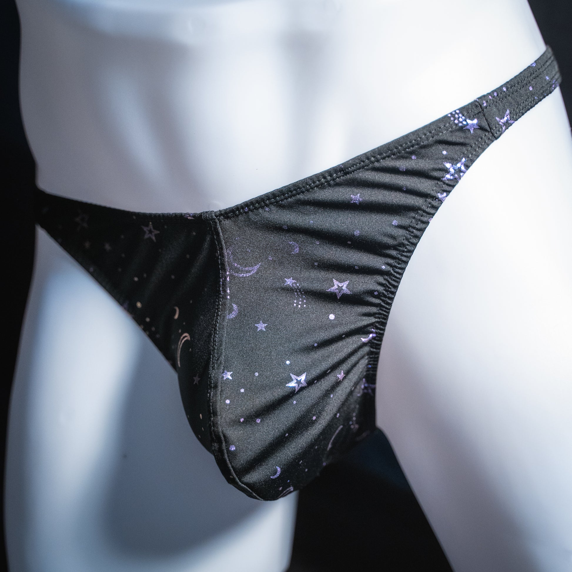 Men's black with purple foil moons and stars thong, classic cut, angled front view.