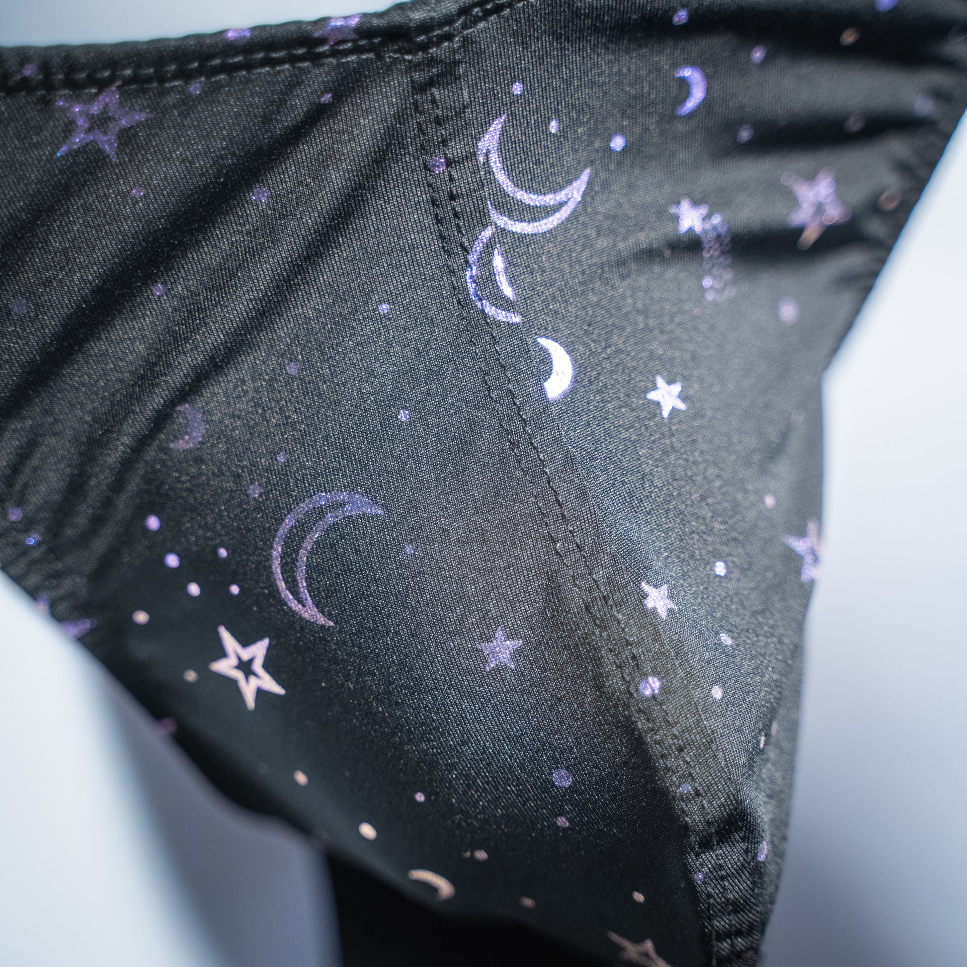 Men's black with purple foil moons and stars thong, classic cut, closeup front view.