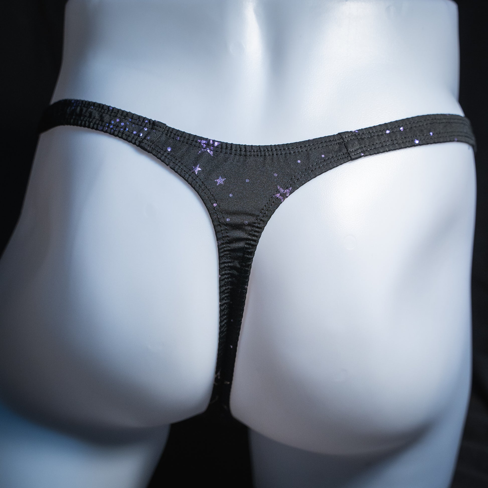 Men's black with purple foil moons and stars thong, classic cut, rear view.