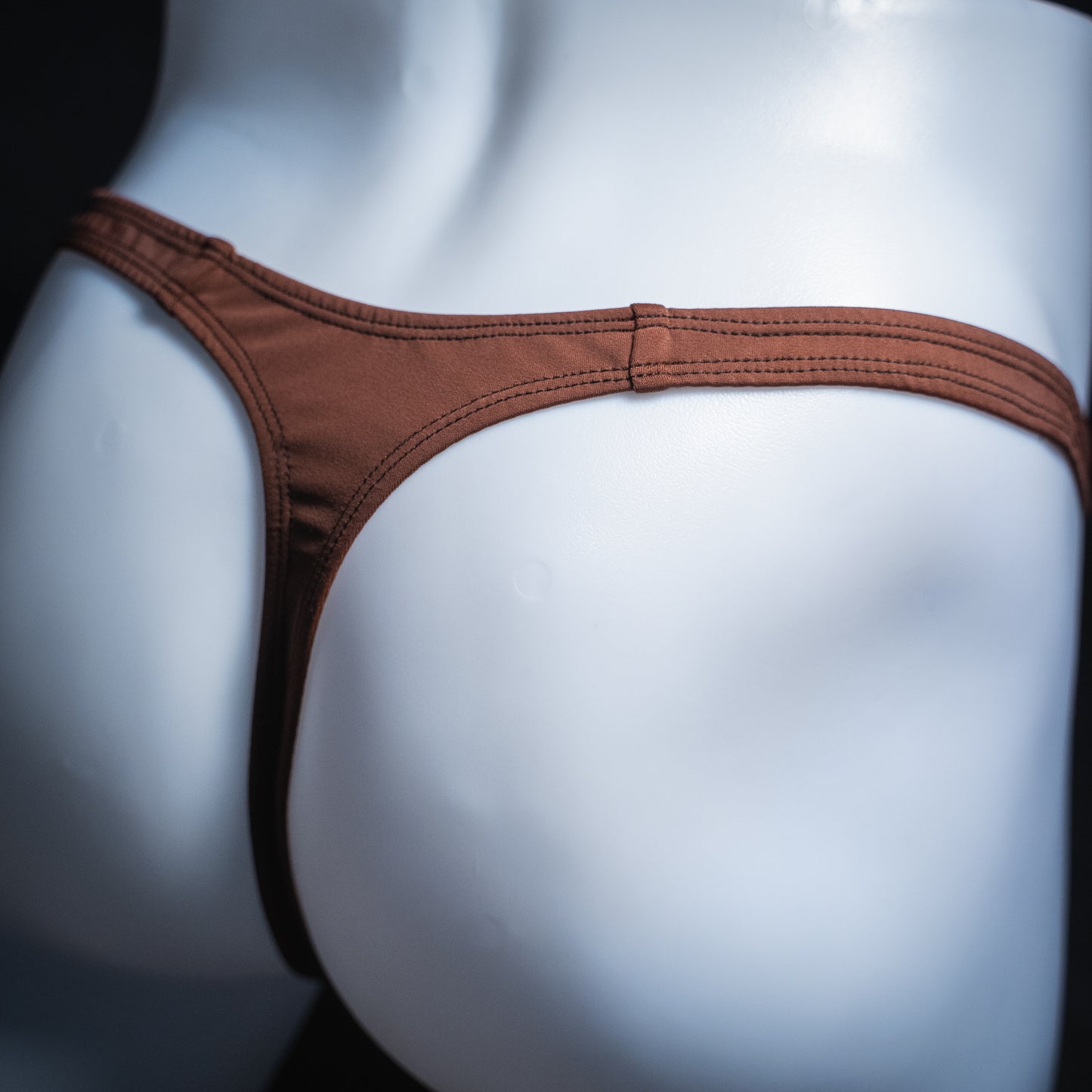 Men's solid brown thong, slim cut, angled rear view.