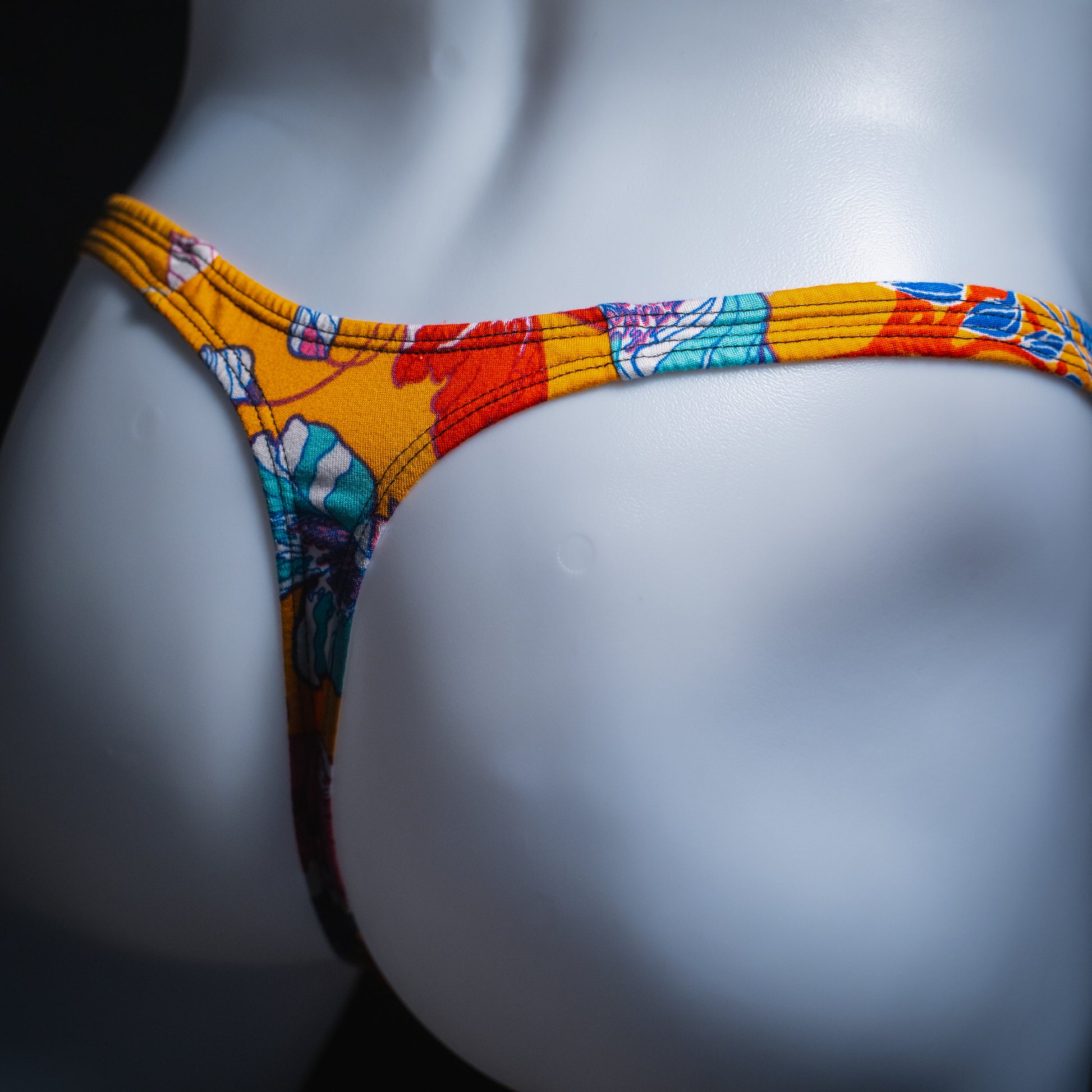 Men's vintage orange floral thong, slim cut, angled rear view.