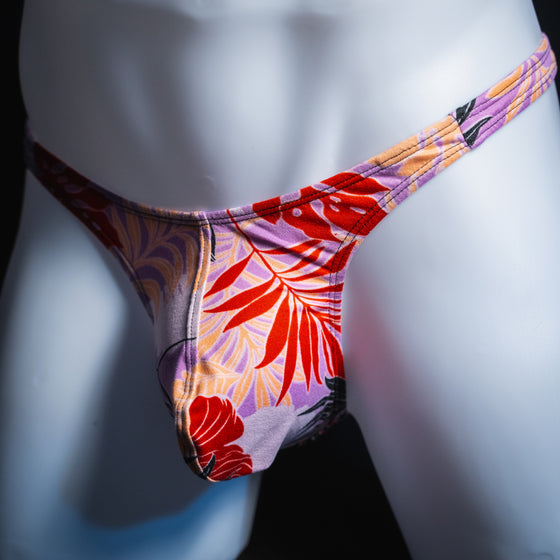Men's vintage purple Hawaiian floral thong, slim cut, angled front view.