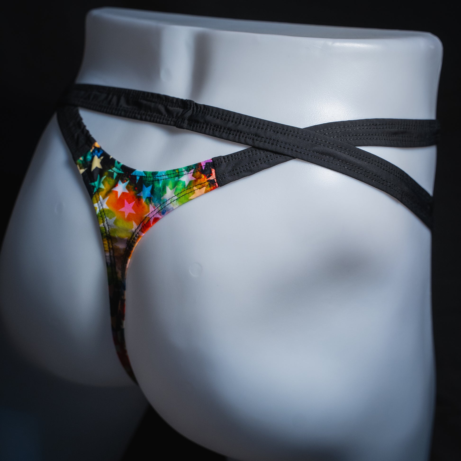 Men's double strap thong with star pattern, slim cut, angled rear view.