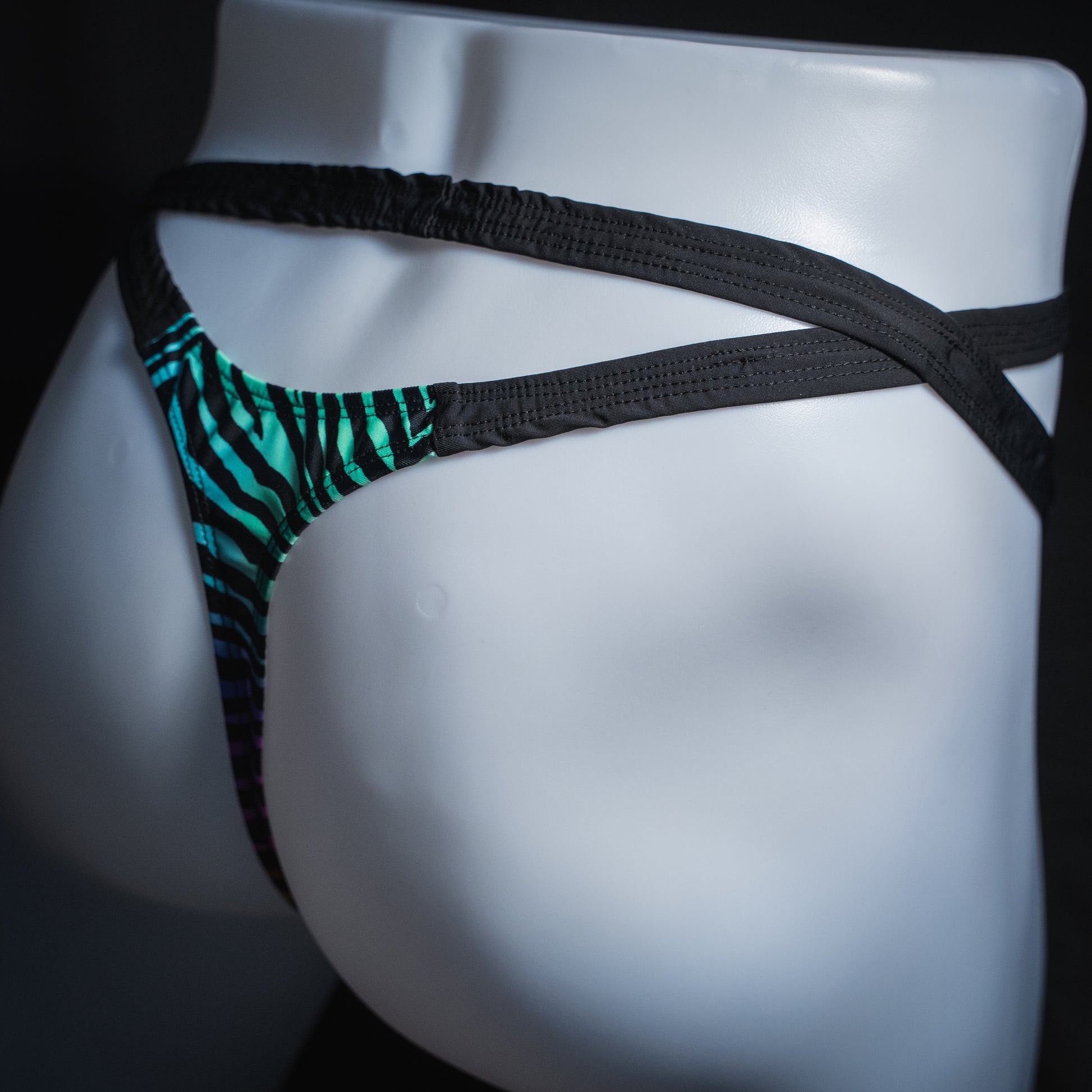 Men's rainbow zebra double strap thong, slim cut, angled rear view.