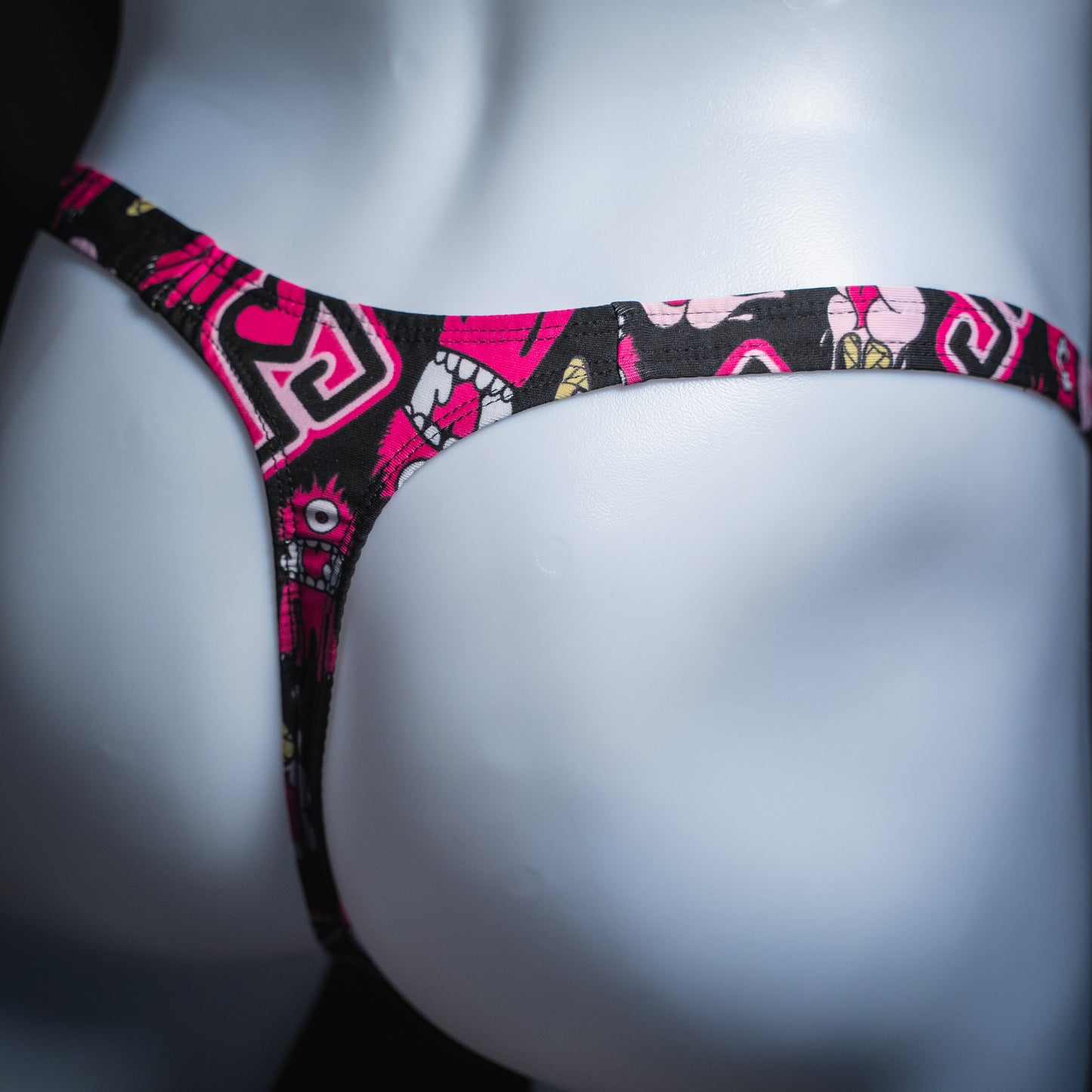 Men's pink monsters on black thong, slim cut, angled rear view.