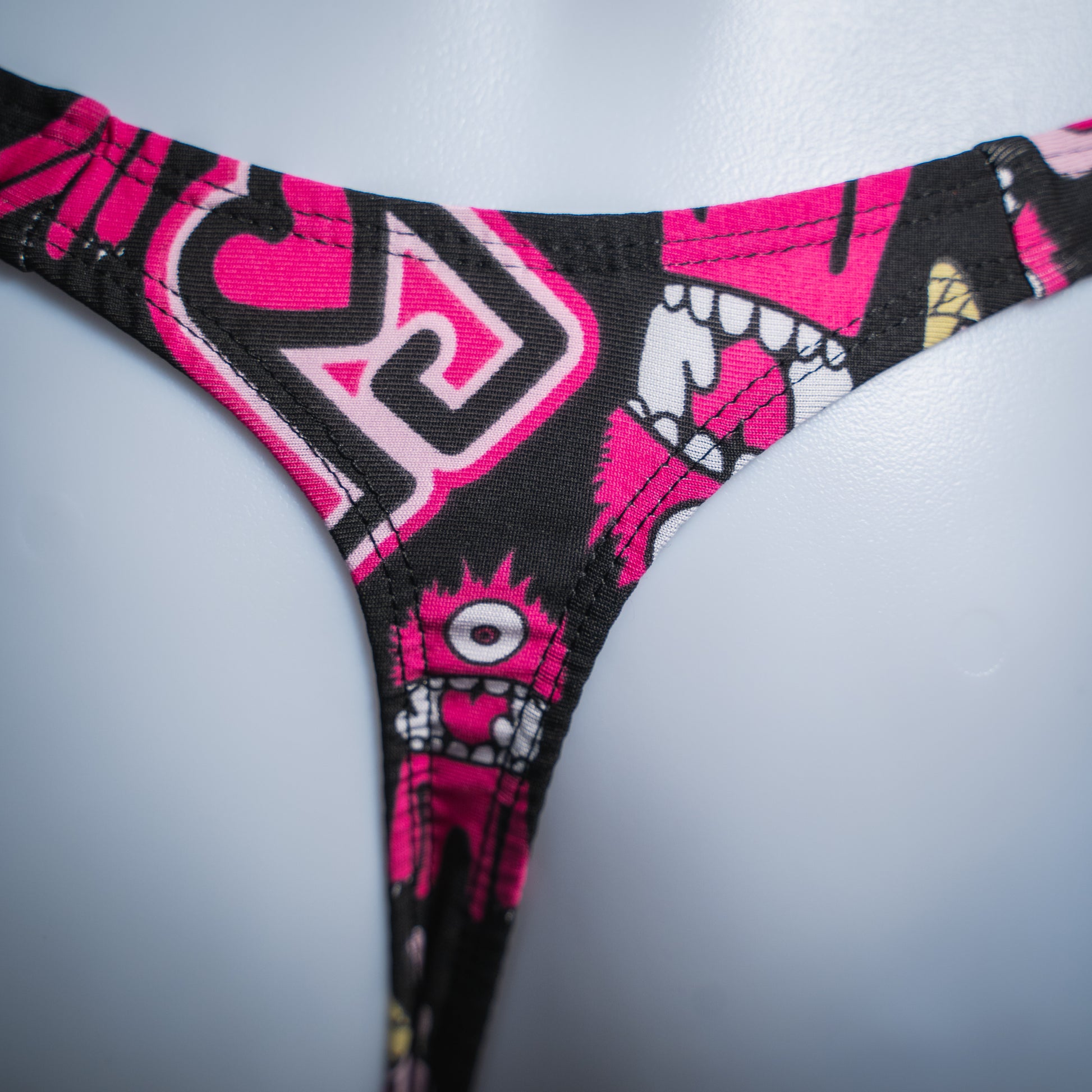 Men's pink monsters on black thong, slim cut, rear view closeup.