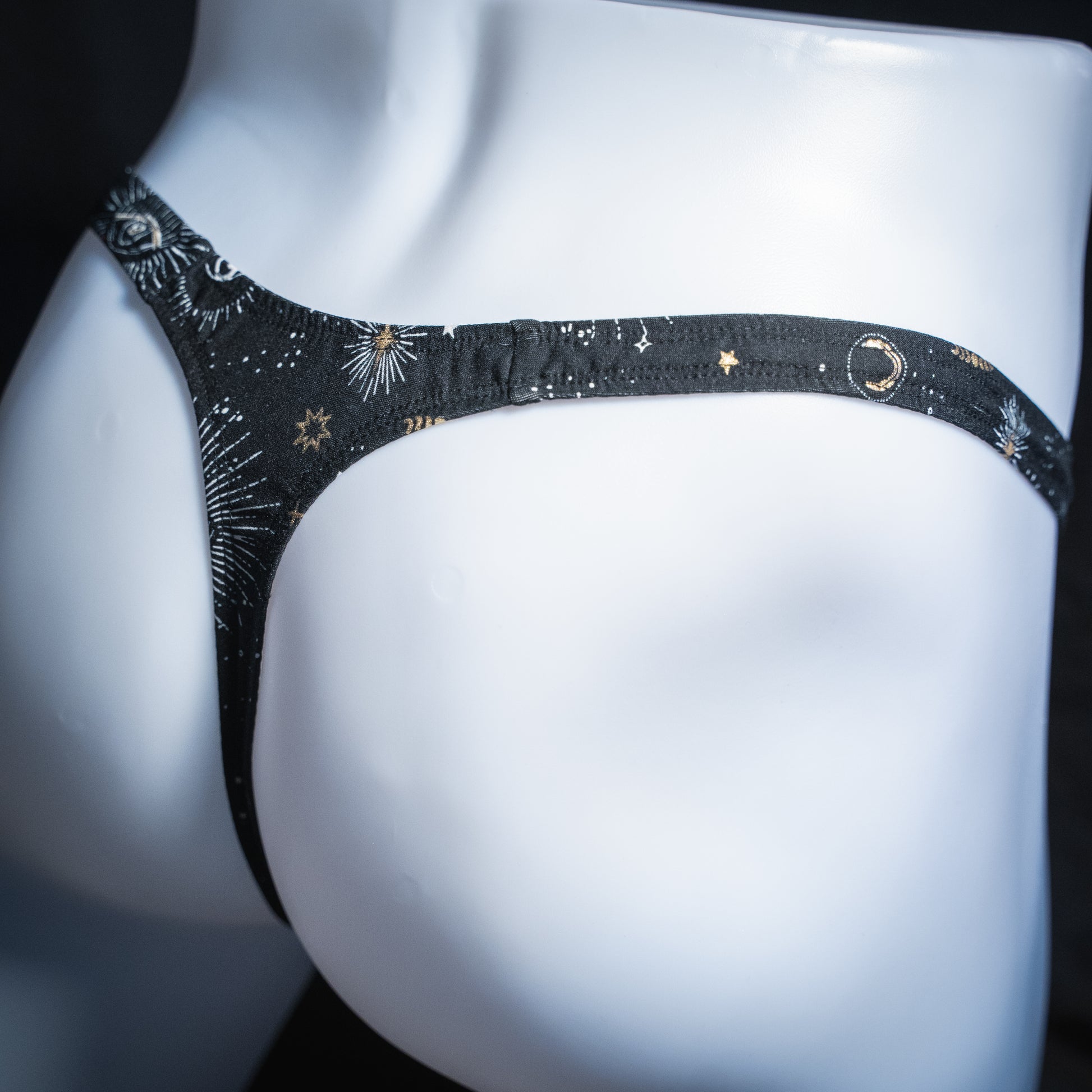 Men's black with supernatural eyes thong, slim cut, angled rear view.