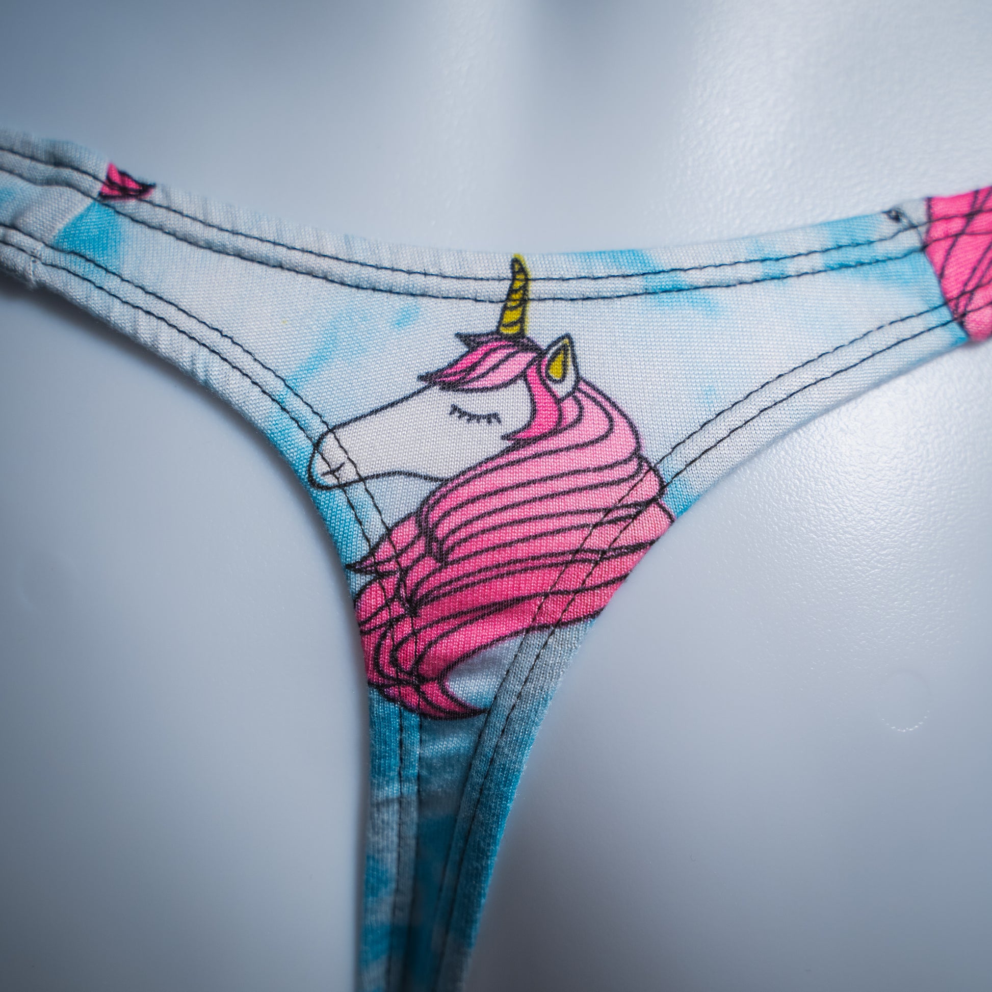 Men's blue clouds with pink unicorn heads thong, slim cut, closeup rear view.