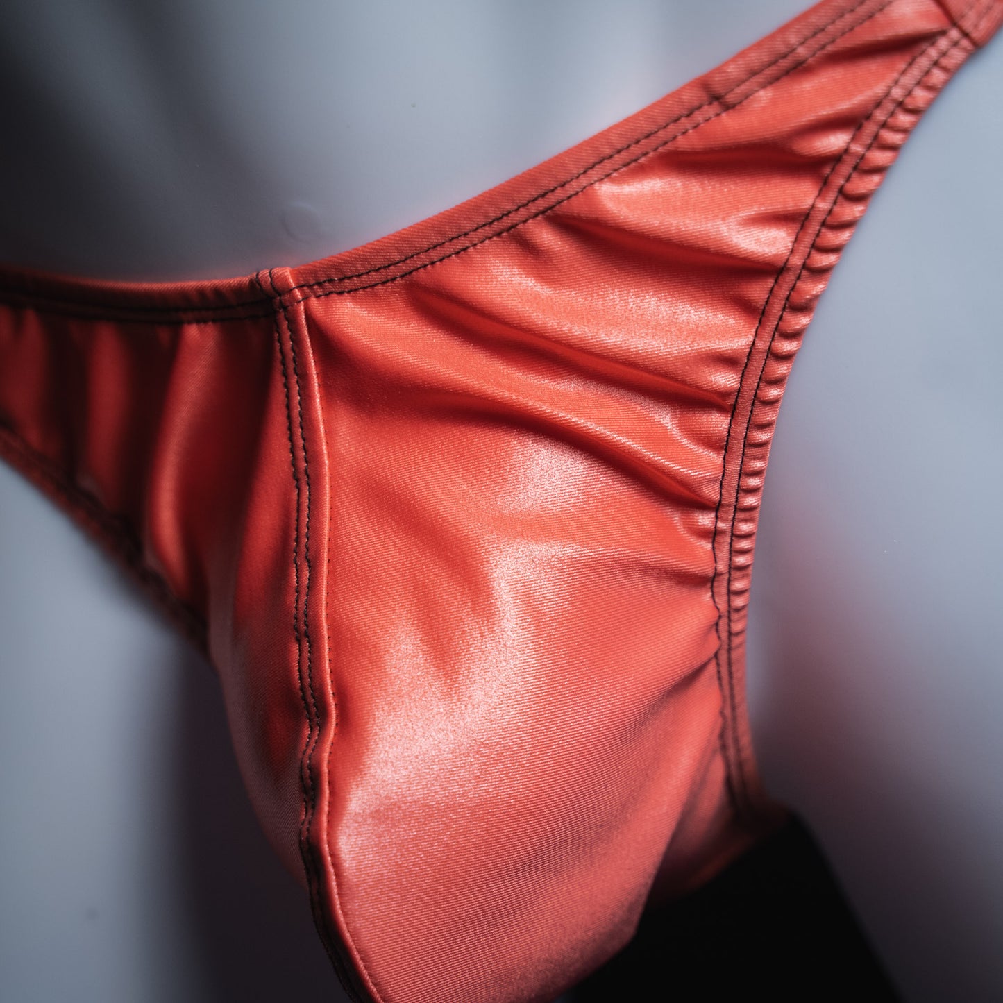 Men's coral pink wet look thong, classic cut, closeup view.