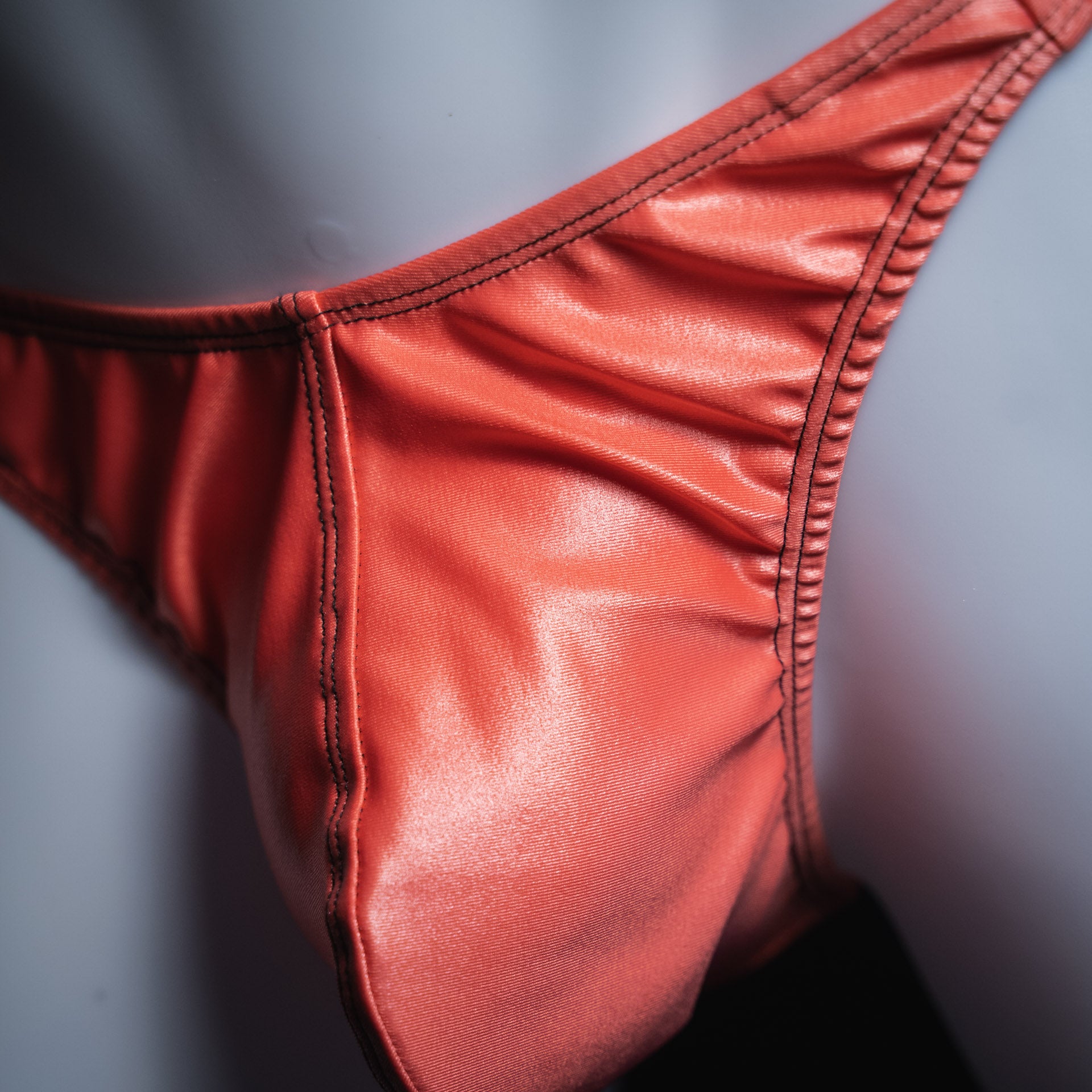 Men's coral pink wet look thong, classic cut, closeup view.