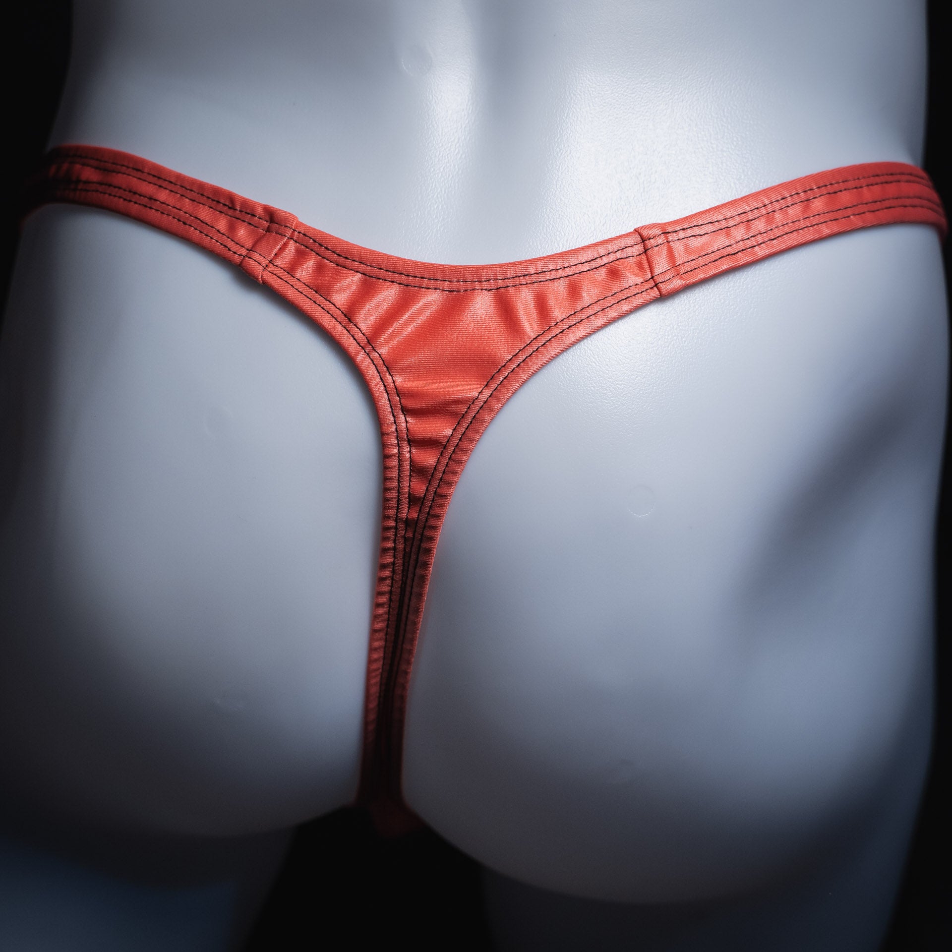 Men's coral pink wet look thong, classic cut, back view.